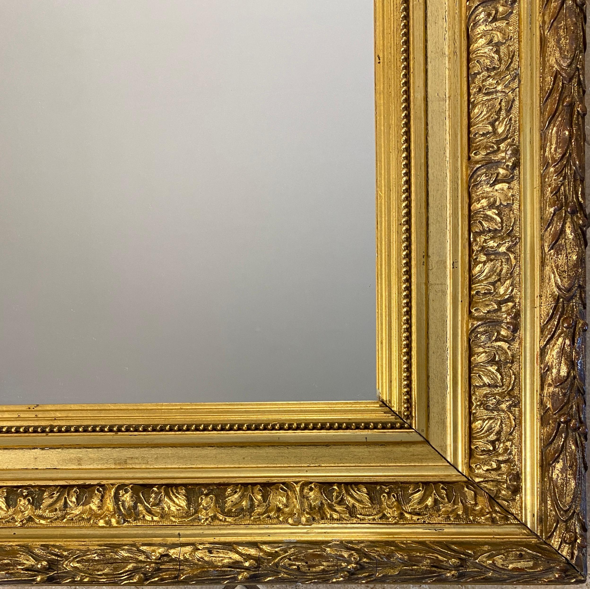 A generously sized rectangular Louis XVI style mirror featuring an intricately carved giltwood frame with an exceptional level of detail. It reflects the grandiose, ornamental Louis XVI style, and it includes an array of period motifs. Its finely