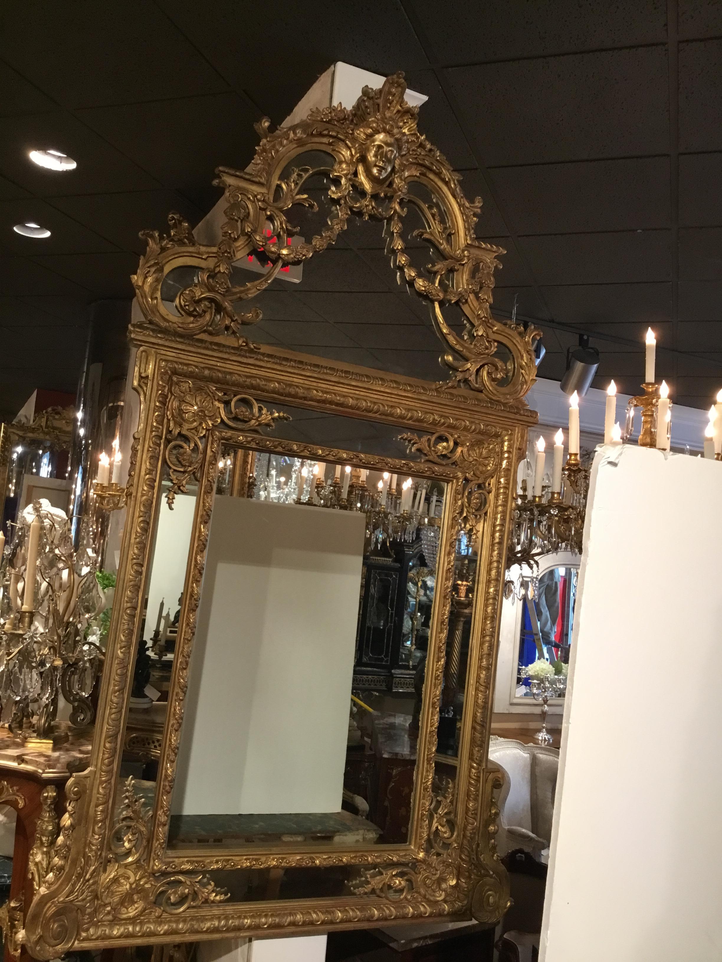 A mask of Minerva is centered at the crest of this monumental mirror.
En chapeau cornice continues with bell flower garlands and foliate carving, gently scrolling curved  framing decorates the sides. The mirror has a second interior frame cushioning