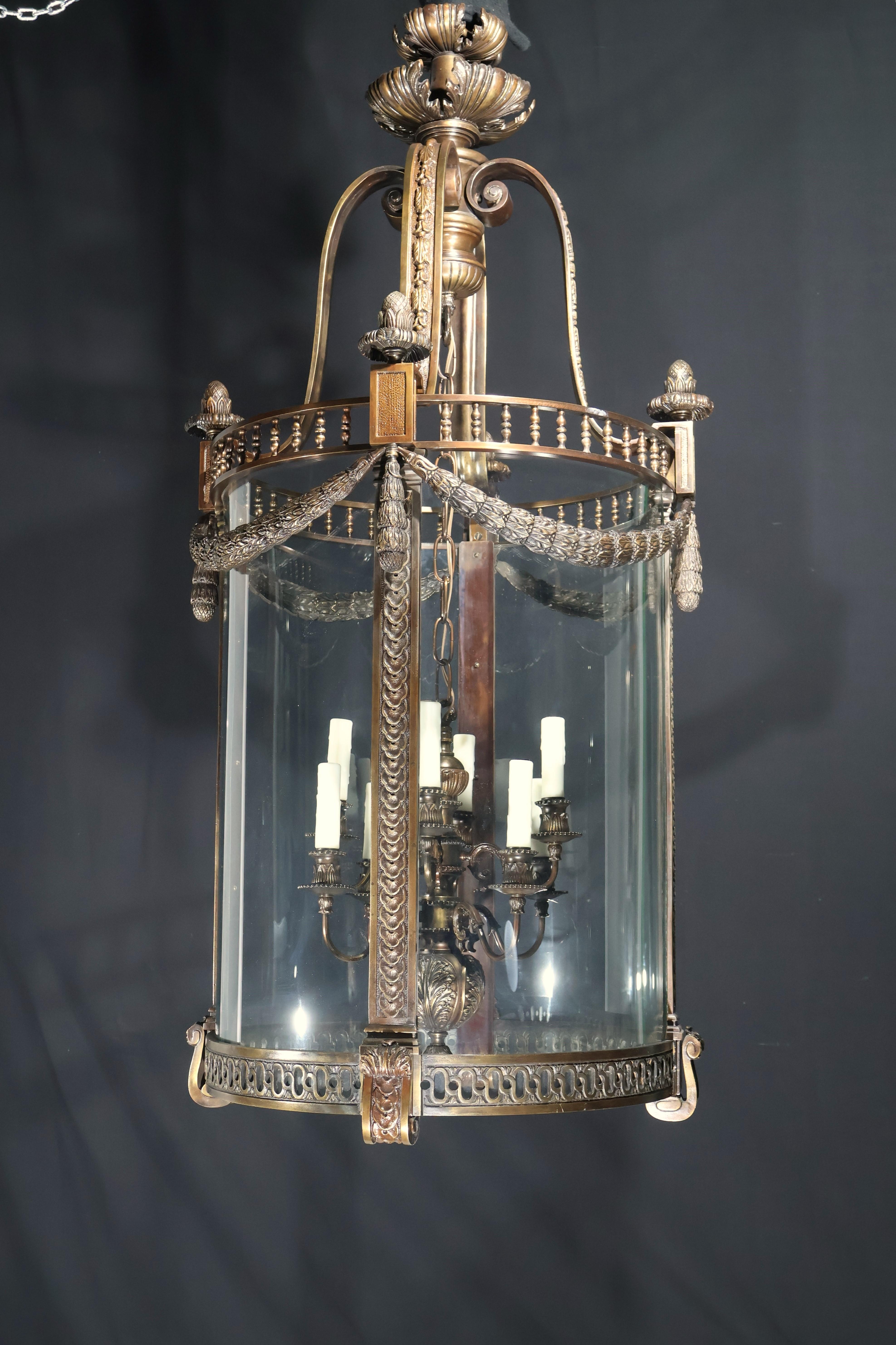 A Magnificent Large Lantern in the Louis XVI Neoclassical Taste, having a curved bronze on bronze - tone metal frame, pinecone finials, laurel swags, all of great quality. Conforming original glass panels. 

Dimensions: (to ring) Height. 56