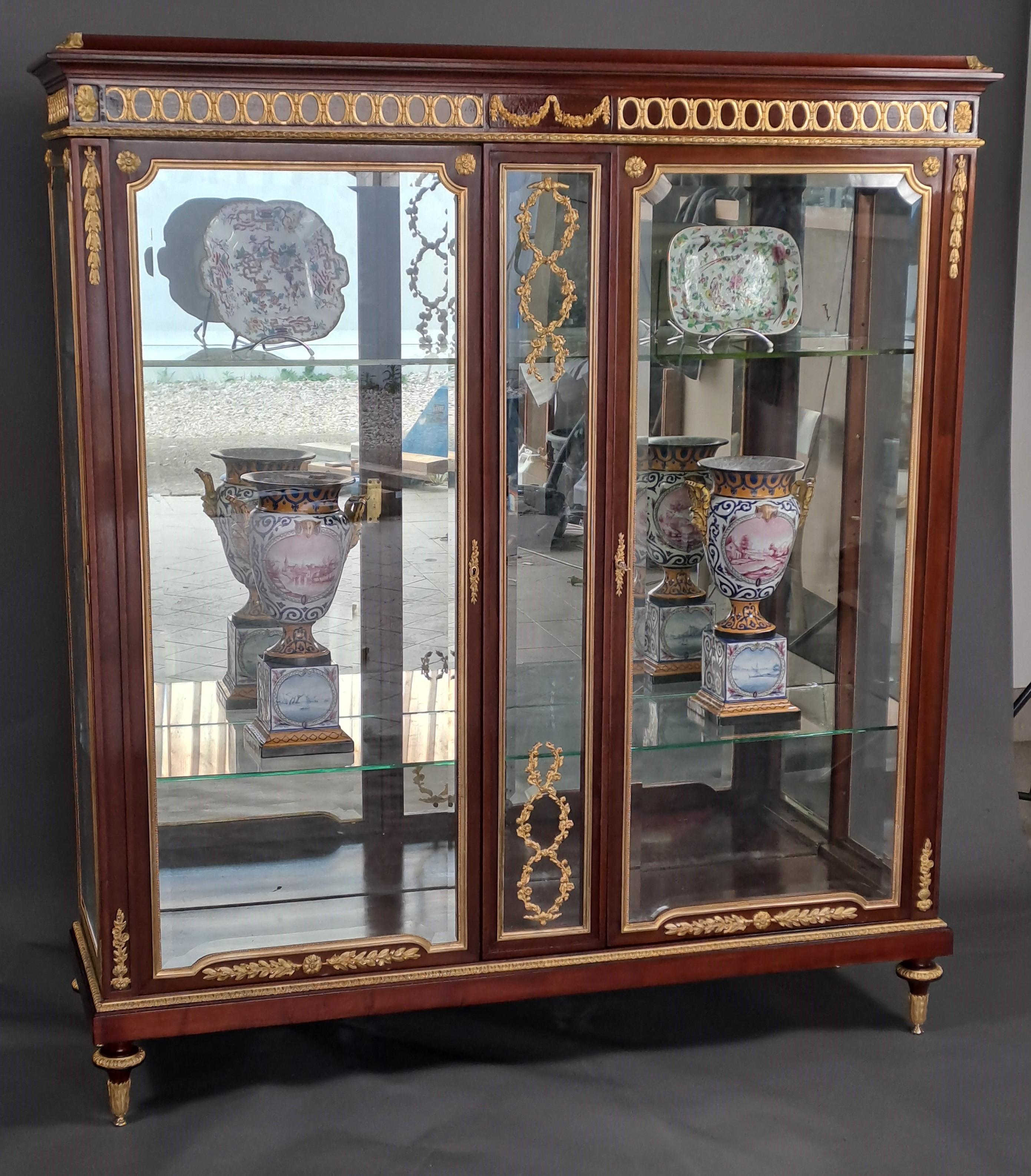 Magnificent Louis XVI style showcase in mahogany veneer with rich, very finely chiseled gilded bronze ornamentation.

Opening two large doors on the front separated by a glass frame.

Beveled windows on the front as well as on the sides.

Mirror