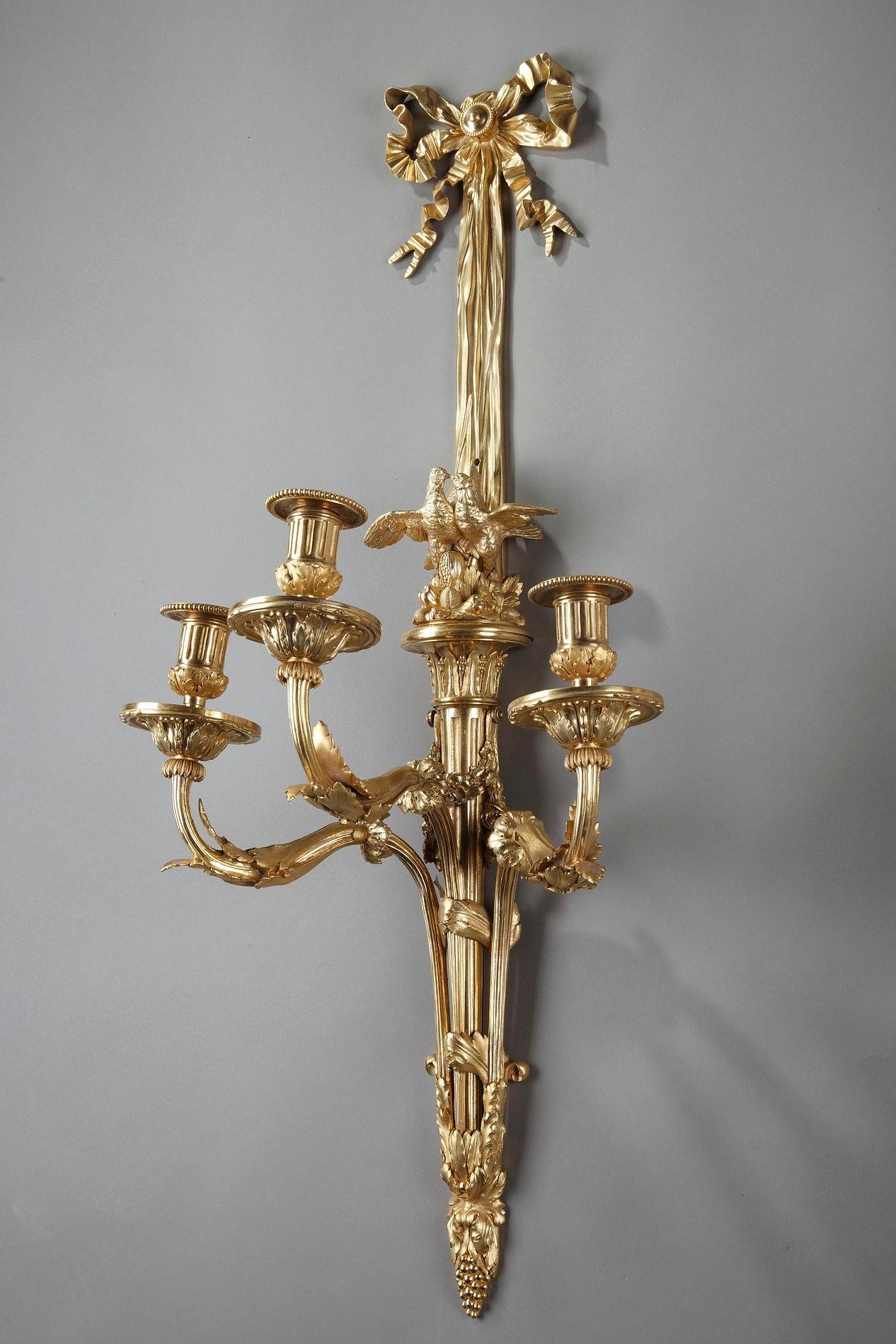 Pair of Louis XVI-style wall sconces crafted entirely of gilded bronze, with three-light decorated with acanthus leaves. The fluted stem highlighted with birds on a fruit basket, is surmounted by a long, descending ribbon bow. Napoleon III