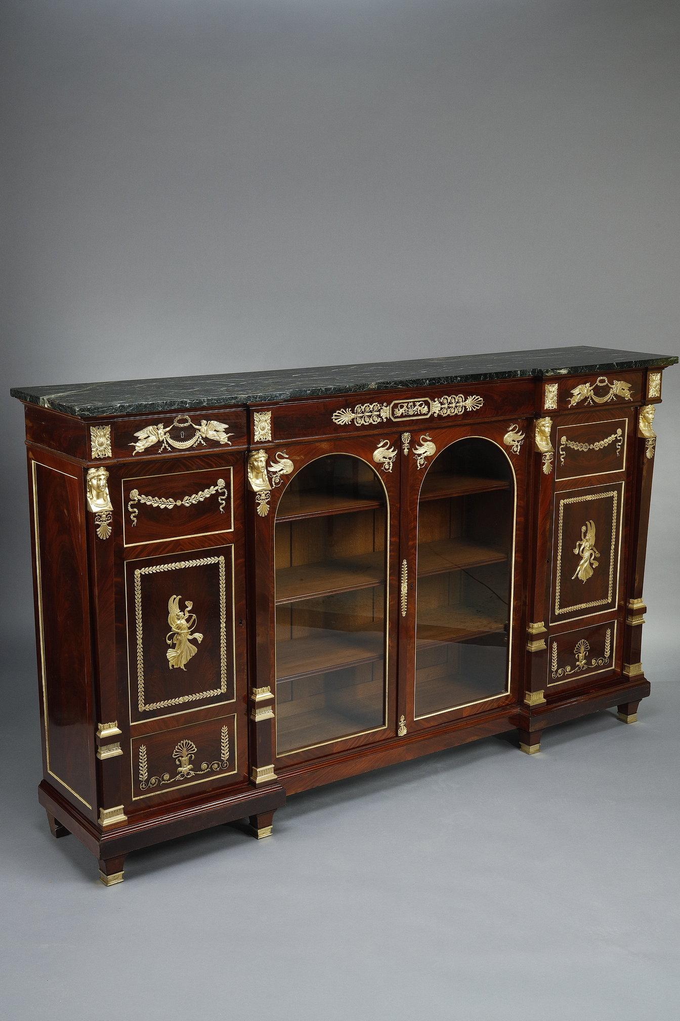 Gran librería baja de caoba y chapado de caoba, abierta con dos puertas completas y dos puertas centrales de cristal en forma de arco apuntado, para exponer libros o coleccionables. Rica ornamentación de bronce, con figuras aladas (Victoire o Niké)