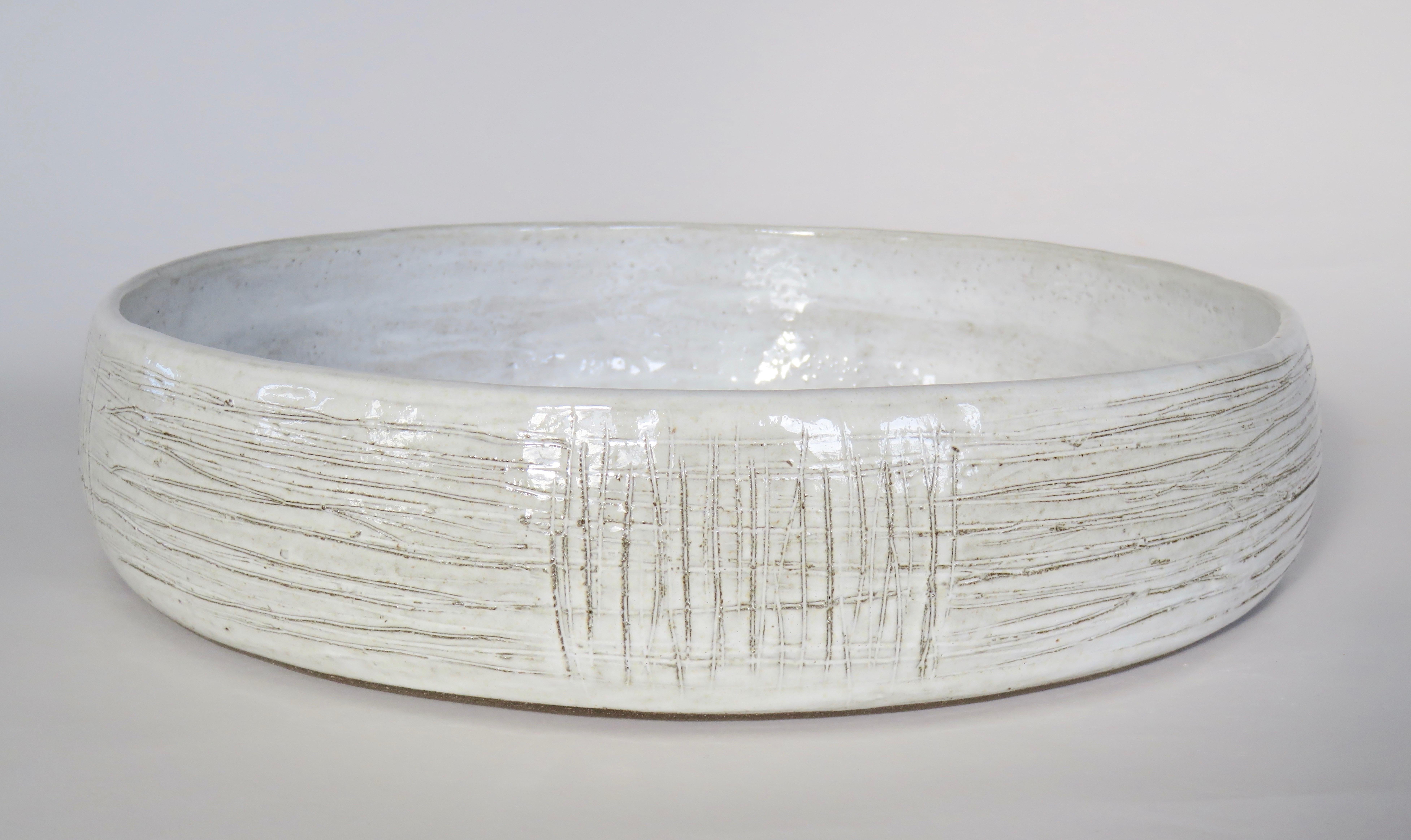 Large, wide and low ceramic stoneware serving bowl and center piece, 14.5 inches in diameter. Distinctive hand carved geometric lines on the outside and a glossy white glaze, reveal the dark clay body underneath.
Fully handmade. Each one is