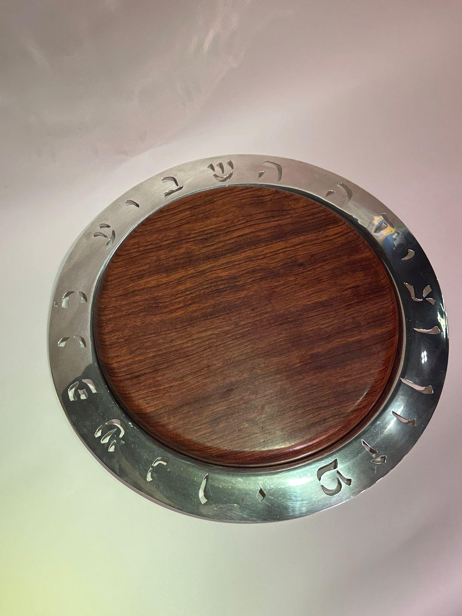 Gran bandeja redonda de plata de ley Kudwig Wolpert con decoración de oración hebraica calada en el borde y una tabla de cortar de madera. En el centro de la parte posterior está marcado 'Wolpert'. Las palabras hebreas perforadas alrededor de la