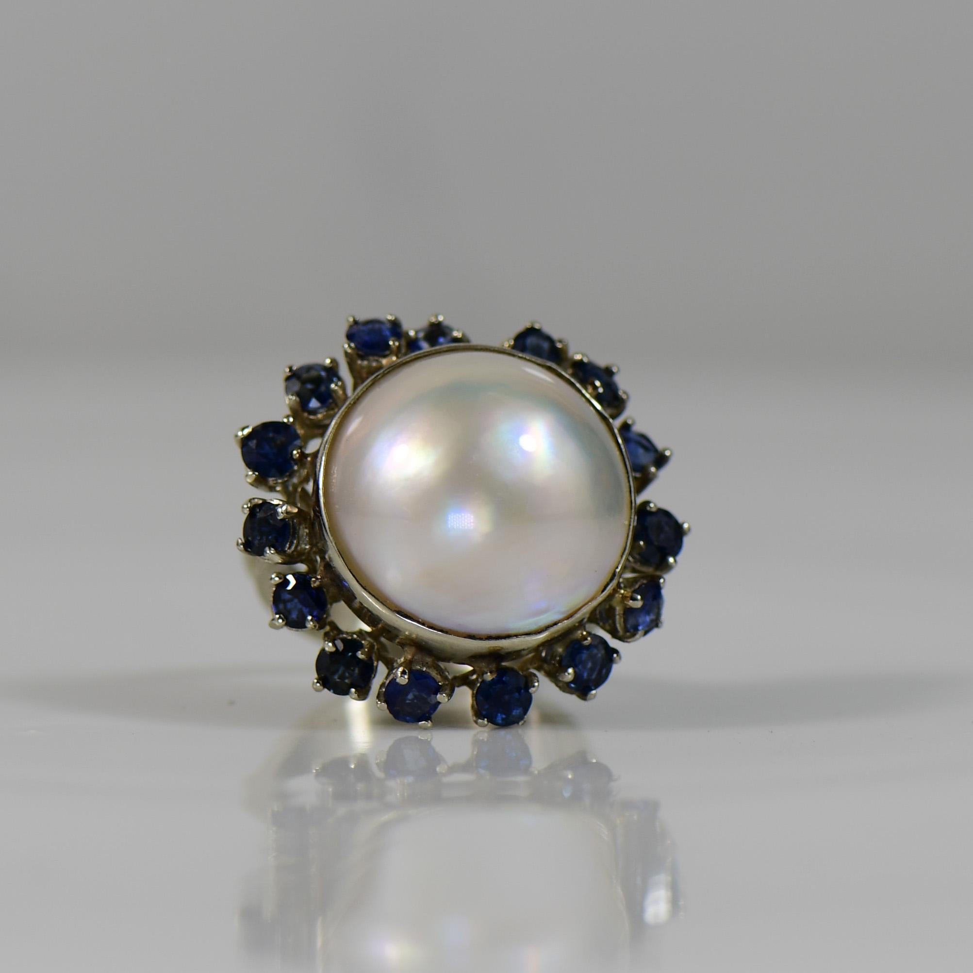 Elegance meets sophistication in this 14K white gold ring featuring a resplendent 18mm pearl as its centerpiece. The lustrous pearl is gracefully accented by a circle of 15 natural sapphires, creating a striking contrast against the pristine white
