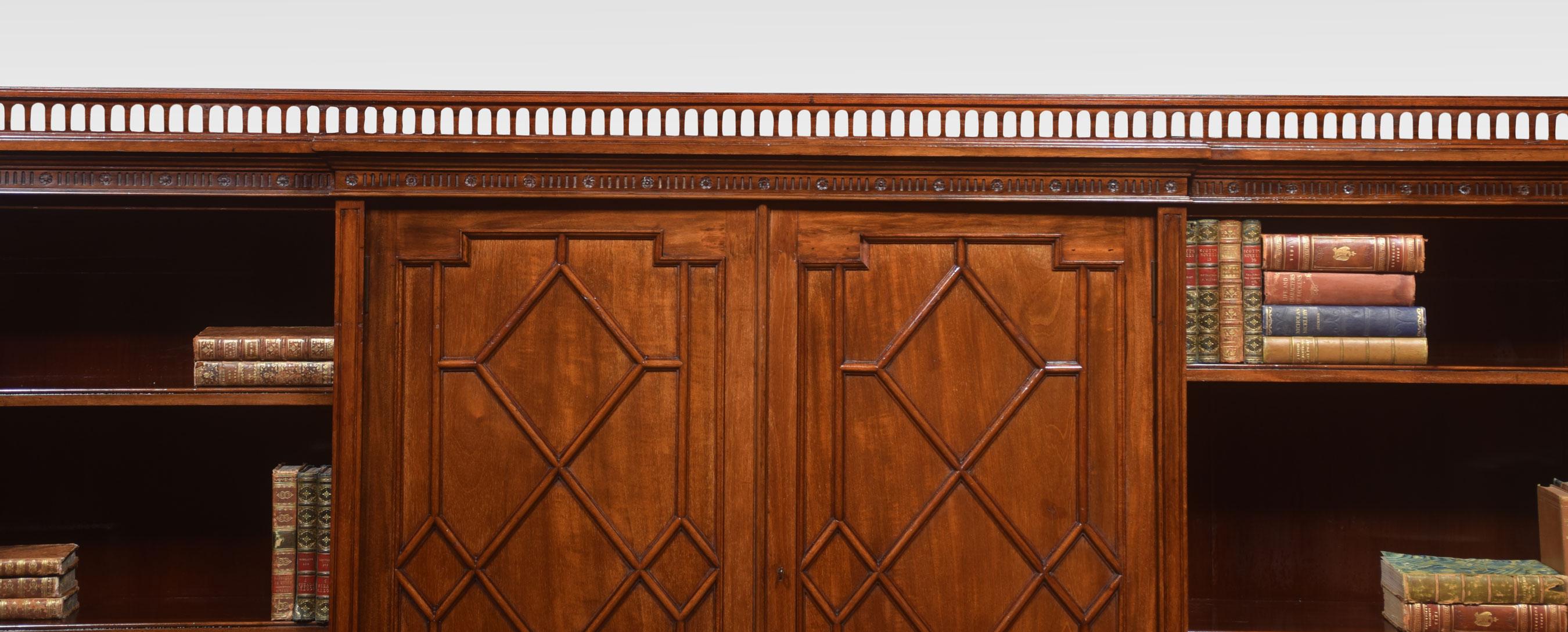 Large mahogany bookcase, having raised turned three-quarter gallery above large rectangular breakfront top. The central panelled doors with moulded lozenge decoration, flanked by two bays of adjustable shelves. All raised up on spade