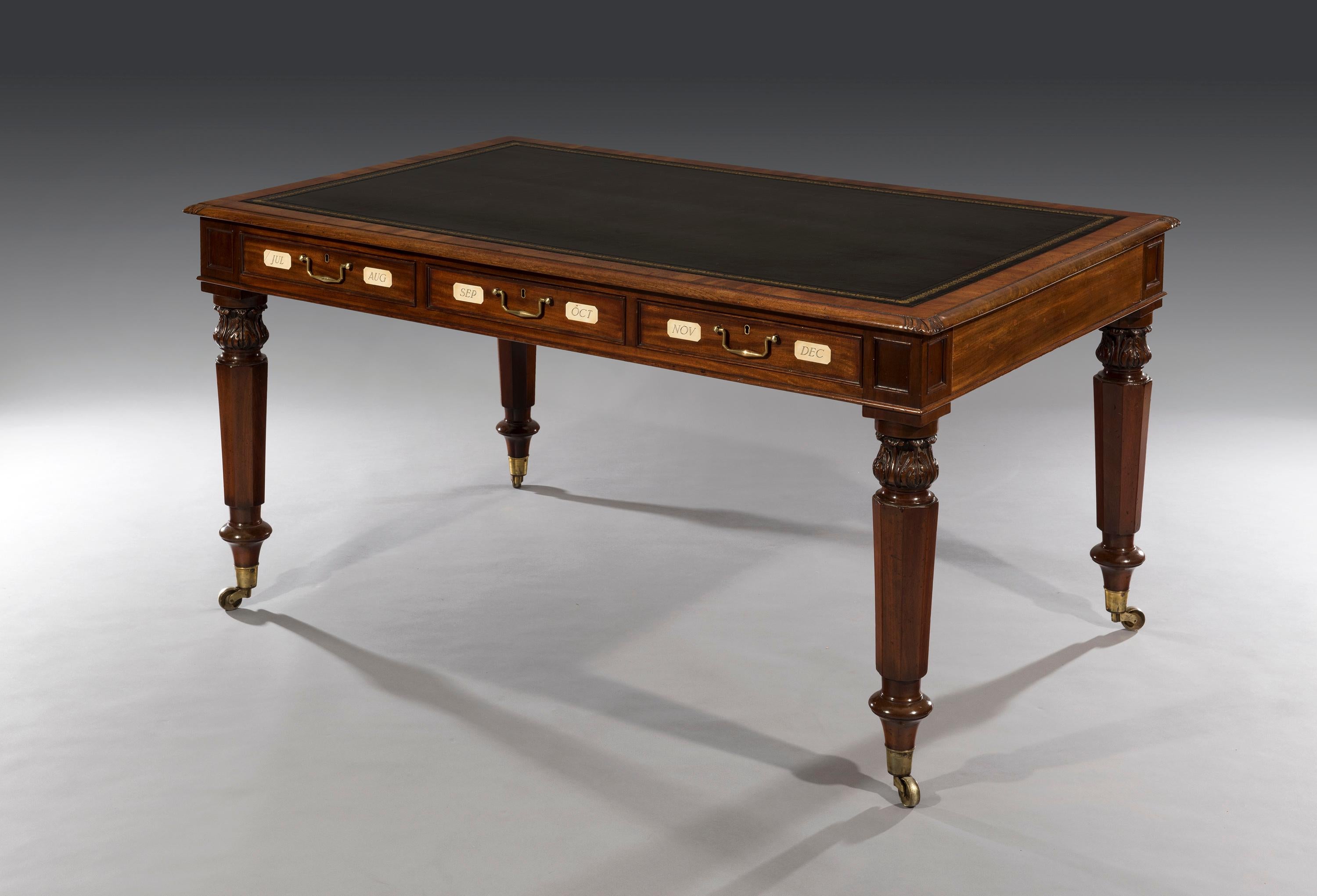 The six-drawer writing table has a black rectangular top above three drawers to the front and three to the reverse. The oak-lined drawers are mahogany fronted with the months of the year inscribed on bone plaques. The frieze has inset panels above