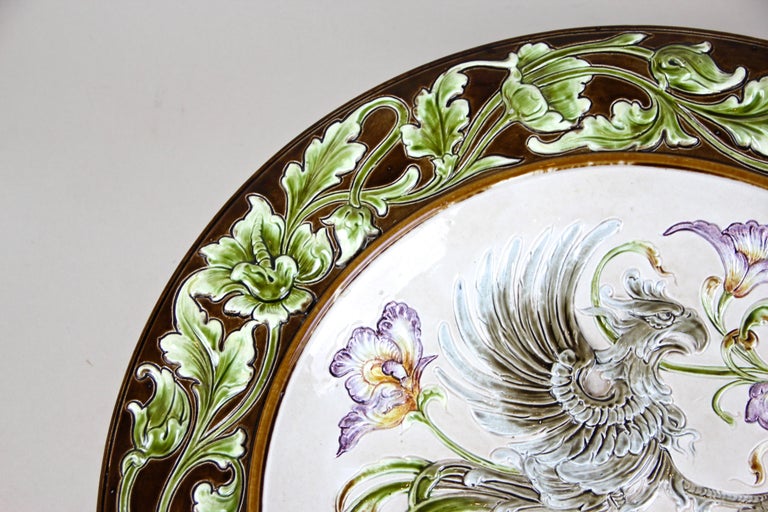 Large Majolica wall plate by the famous company of Wilhelm Schiller & Son from circa 1890. Showing a grey griffin which holds a blue/white coat of arms and gorgeous floral design in relief, this late 19th century Majolica Plate comes with a dark
