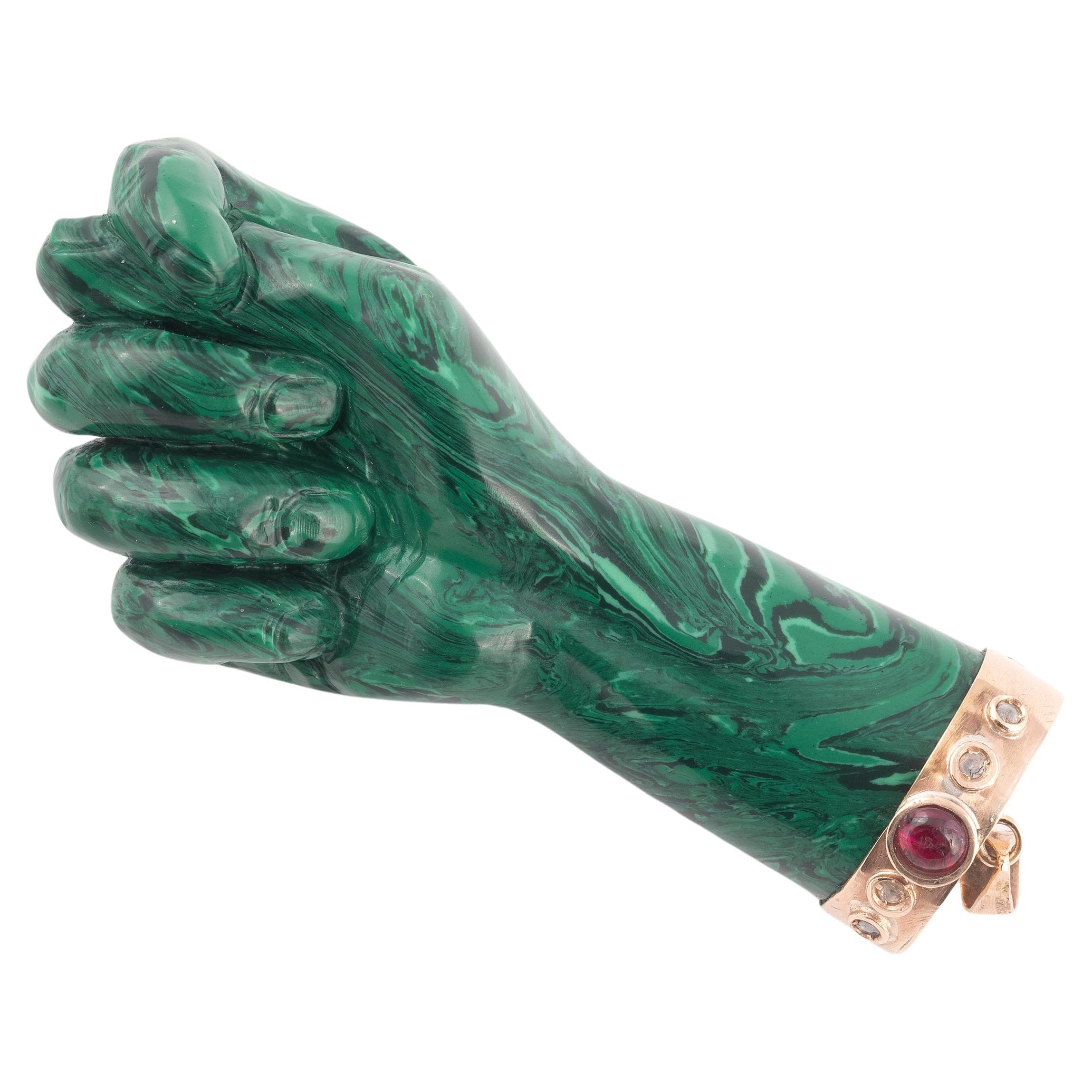 The malachite and realistically modelled with the thumb between the first two fingers surmounted by a gold cap embellished with cabochon cut semi-precious stones, length 80mm including loop.
Weight: 41gr.
A higa jewel (sometimes known as a figa)