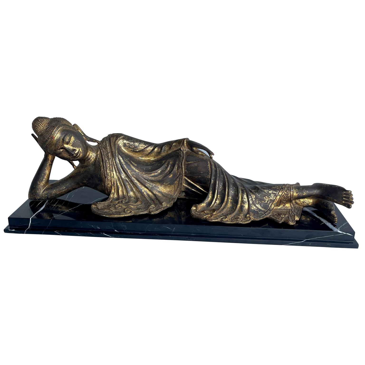 Antique Mandalay Style Gilt Bronze Sculpture of Reclining Buddha on a Heavy Solid Rectangular Profiled Black Marble Base.
The reclining Buddha is draped in a robe with highly detailed forged folds of fabric, and leaving the right shoulder exposed,