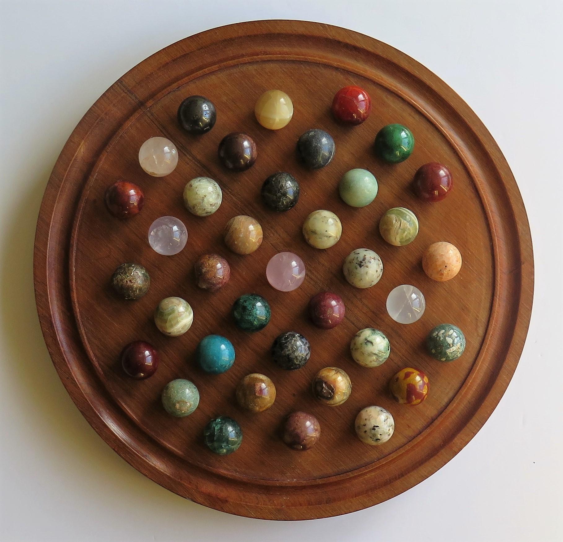 This is a very decorative and complete board game of 37 hole marble solitaire with a large 12.75 inch diameter hardwood board and 37 beautiful individual mainly mineral or agate stone and some glass marbles, which we date to the early 20th century,