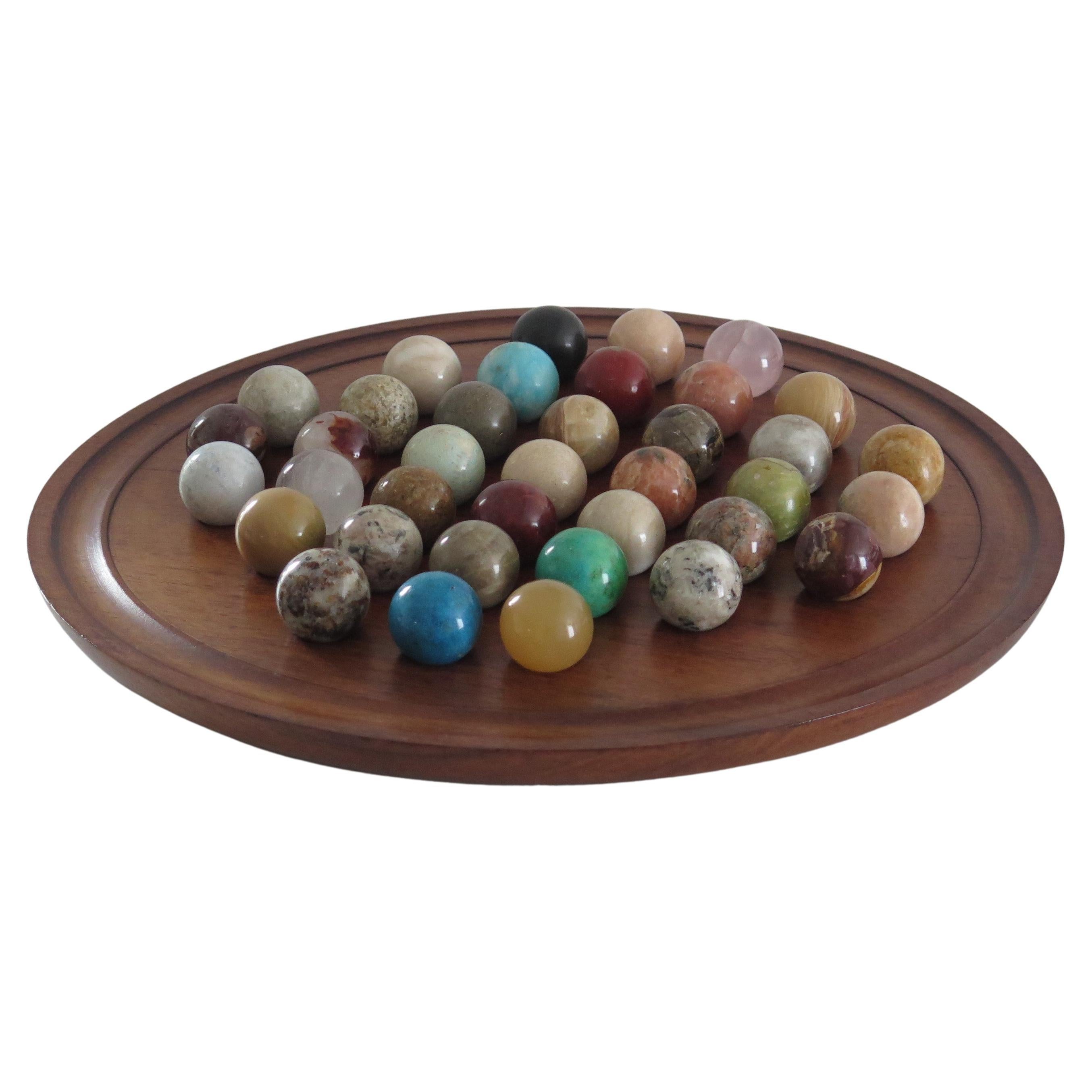 This is a very decorative and complete board game of 37 hole marble solitaire with a very large 14 inch diameter hardwood board and 37 beautiful individual mineral or agate stone marbles, which we date to the early 20th century, probably of French
