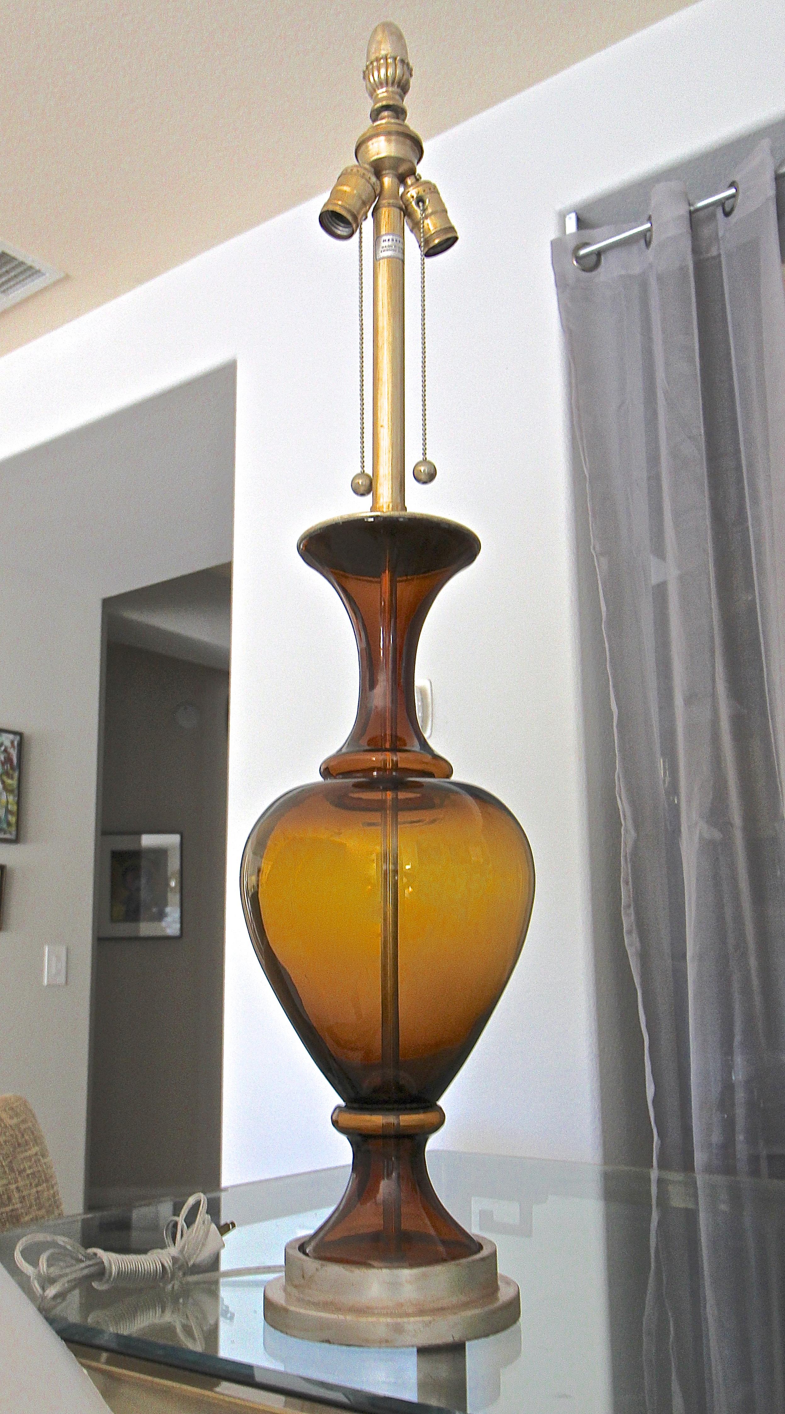 Large hand blown Marbro lamp with root beer colored blown glass body mounted silver giltwood base. Has double cluster antiqued chrome fittings and carved silver giltwood finial. Depending on light source glass color ranges from shades of amber to