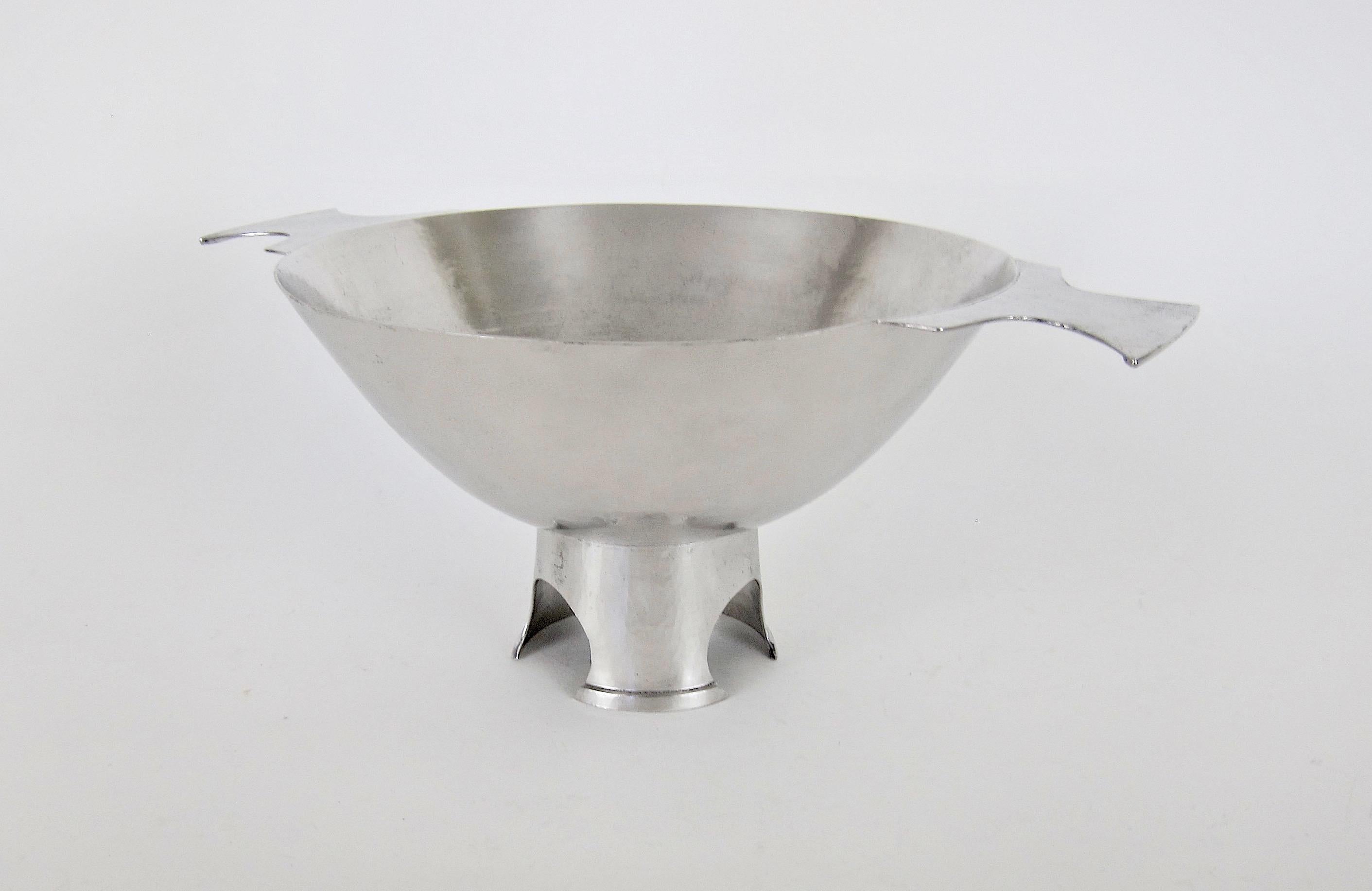 A large double-handled centerpiece bowl in hammered silver metal by American metalsmith, designer and jeweler, Marie Zimmermann (1879-1972) dating to the early 1920s. Zimmermann designed the sculptural footed bowl in the shape of a large-scale