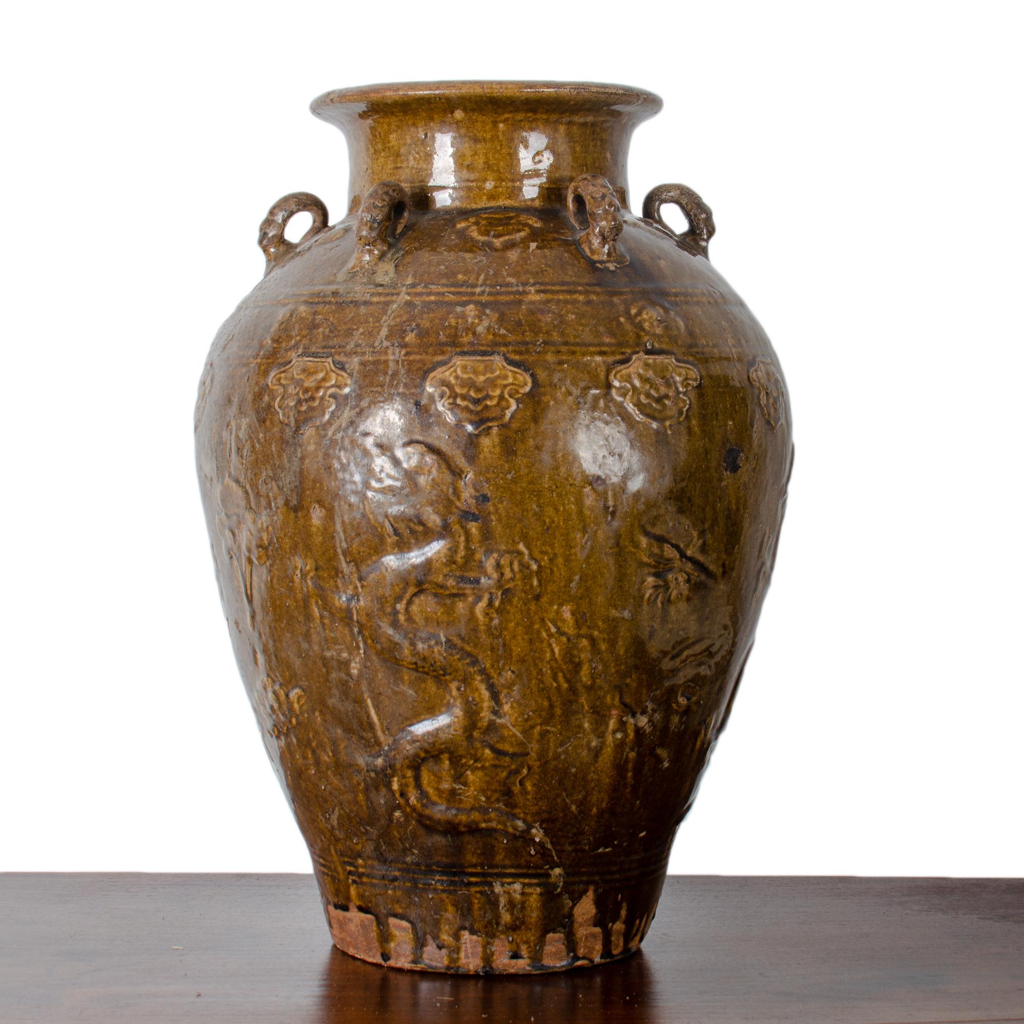 A large brown glazed Martaban storage jar, c. 17th-18th century. 

Tapering ovoid form with molded sides depicting dragons, cranes and floral ornamentation. 

Six dragon head looped straps at shoulder.

22 ¼ inches high by 16 inches wide.

