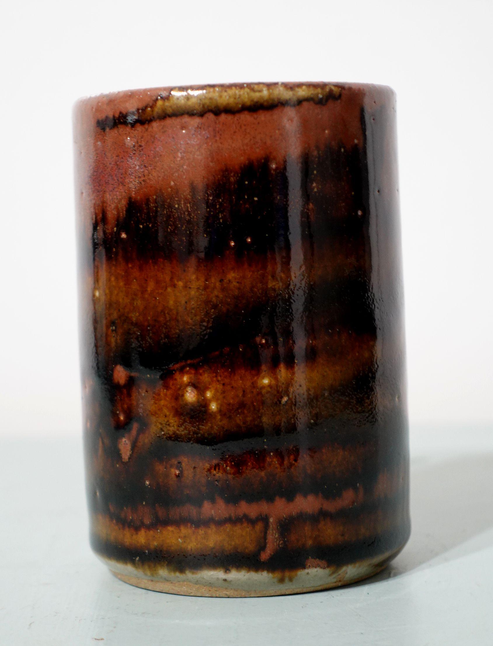 A Japanese Mashiko Cup studio pottery with stylized designs in the brown glazed body in the manner of cloud-water flowing pattern and dating from around the 1950s. The large cylindrical-shaped cup stands on a thick rounded non-unglazed foot with the