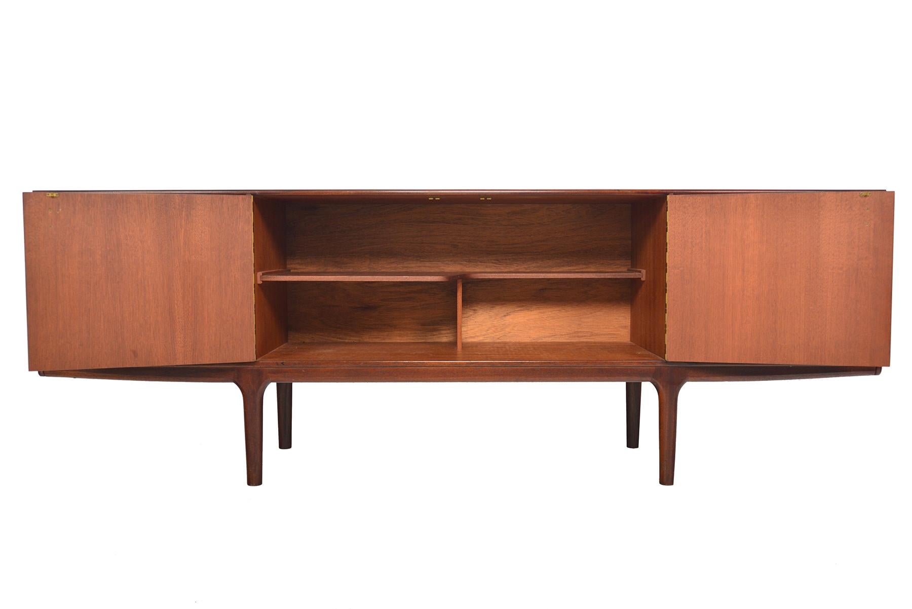 This Mid-Century Modern “Dunottoer” model large low line rosewood sideboard by A.H. McIntosh was designed in the 1960s. Two center doors open to reveal a fixed asymmetrical bar shelf. Right bar cabinet drops down to reveal open storage with a black