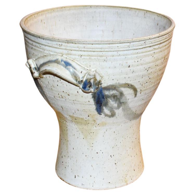 A large earthenware ceramic jardiniere or planter. This piece is decorated with a creamy white and blue design. Each side features an applied free-form handle. This would be great in any space. We love the idea of using it as a planter on a patio,