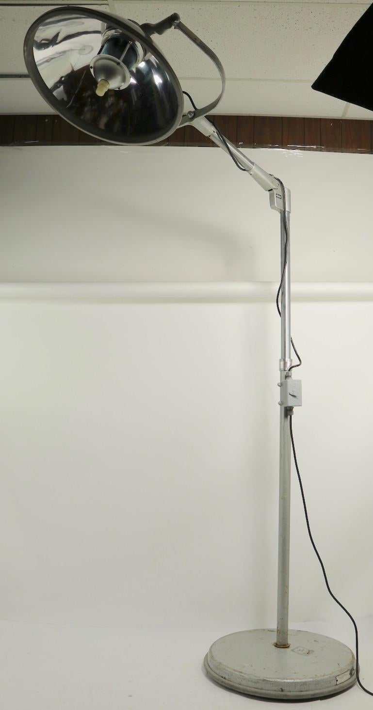 Large and impressive surgical floor lamp by American Surgical Luminaire / Crouse Hinds. The lamp features a reflective dome hood shade (23 inch diameter) which tilts and pivots to direct the light, attached to a pivoting arm, on an extendable