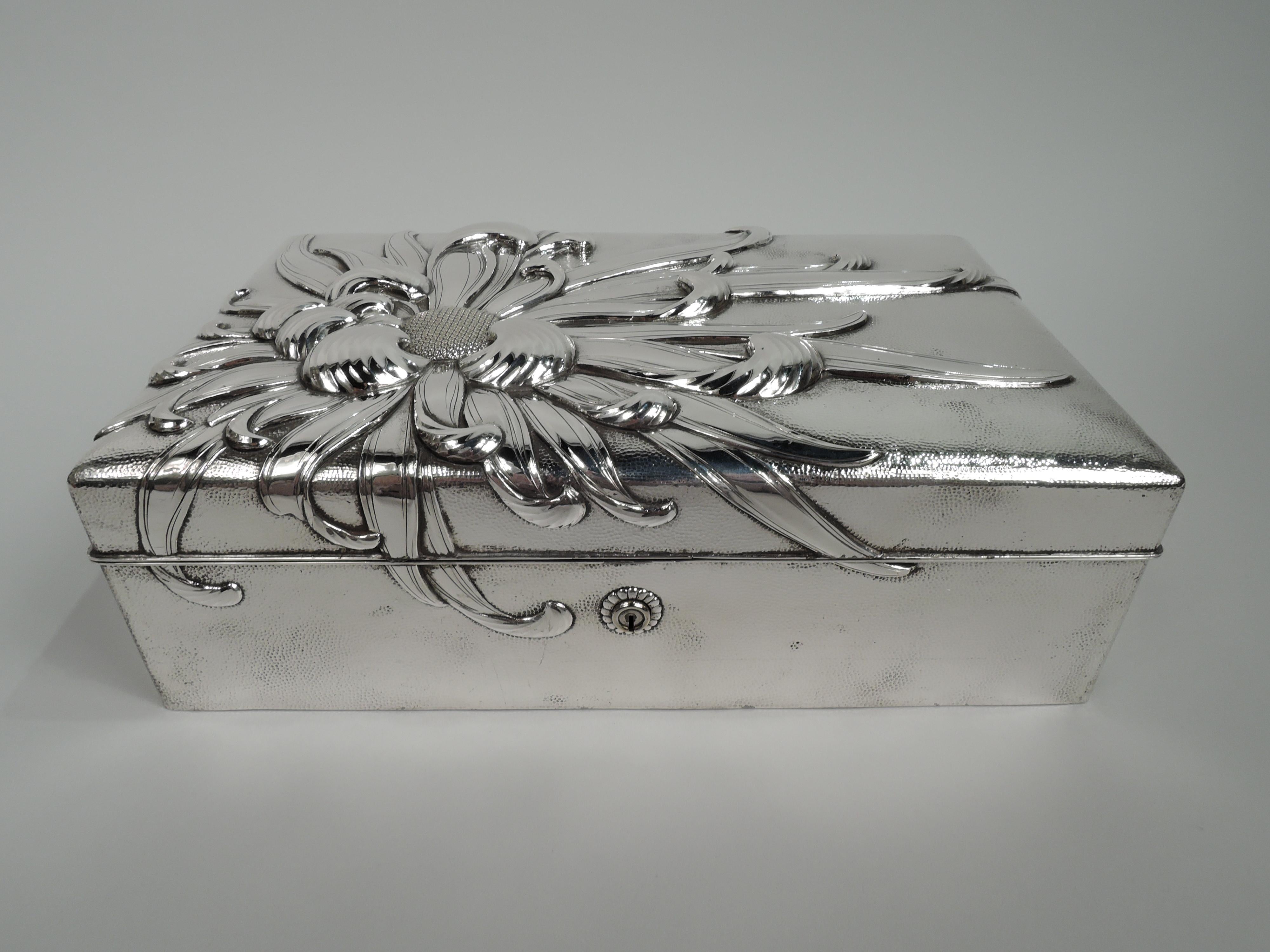 Bold and striking Japanese silver box, ca 1910. Rectangular with straight sides and hinged cover. Allover spot hammering. On cover top is applied chrysanthemum with entwined and waving tentacular petals that drape over the sides. Petal-bordered