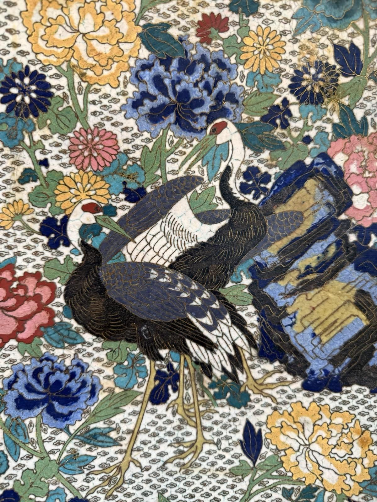 Superbe chargeur en émail cloisonné japonais de la période Meiji, richement décoré, présentant une scène élaborée de deux grues à couronne rouge au milieu de pivoines en fleurs, de chrysanthèmes et de feuillages multicolores. Un papillon finement