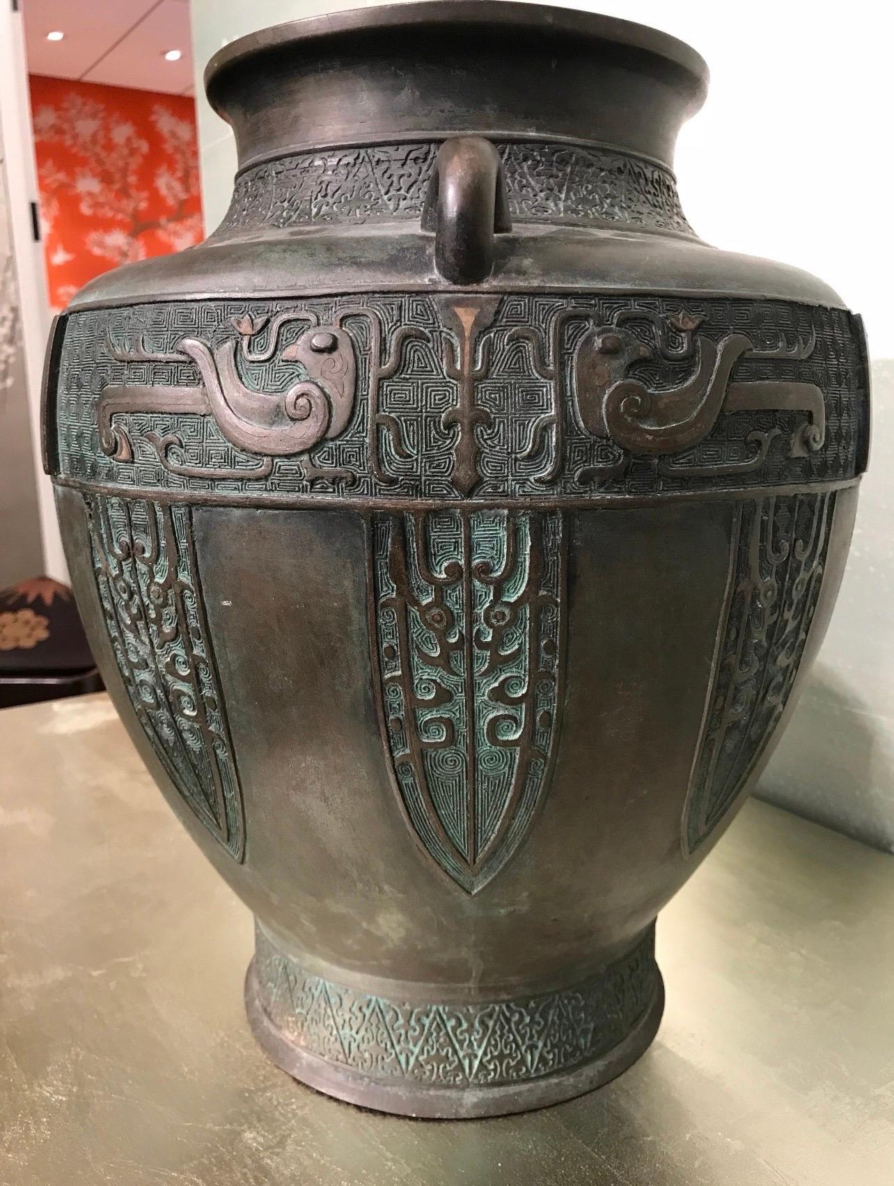 A substantial and beautifully decorated antique Japanese bronze vase in archaic style.

The urn-shaped body is supported on a recessed base, with a rounded shoulder and a short neck ending in a flared rim.

The shoulders are flanked by two handles