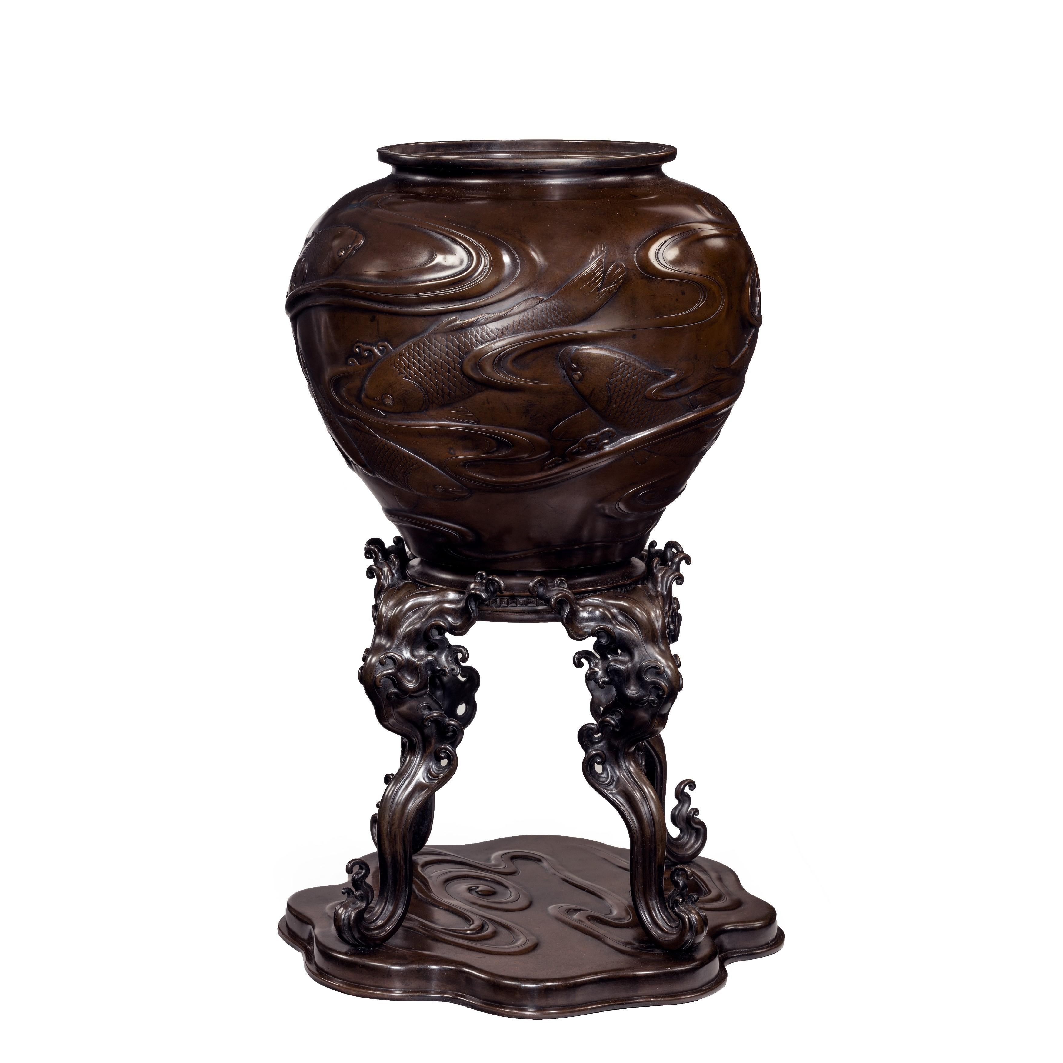 A large Meiji period bronze vase on stand, of globular form decorated with a continuous frieze of carp swimming in swirls of water, with gold-inlaid eyes, the base with four wave and spray legs on a shaped base with further raised ripples, signed