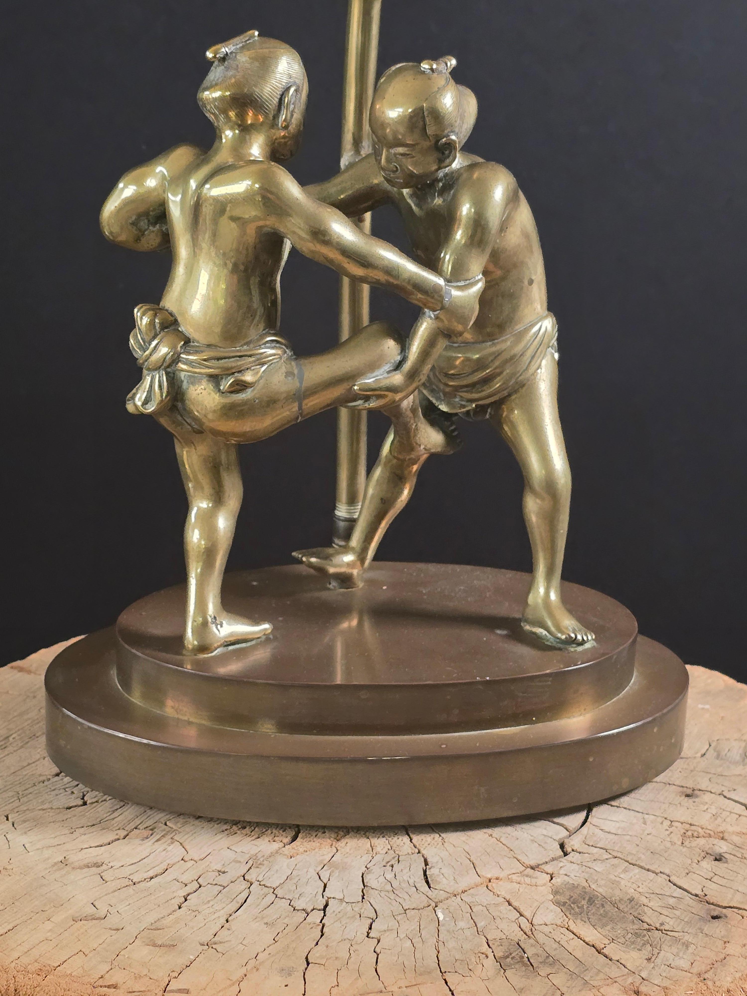 Un lourd bronze japonais coulé en masse représentant deux lutteurs de sumo, finement détaillés avec une musculature tendue, des visages expressifs et des ceintures mawashi traditionnelles. Les figures sont montées comme une lampe sur une base
