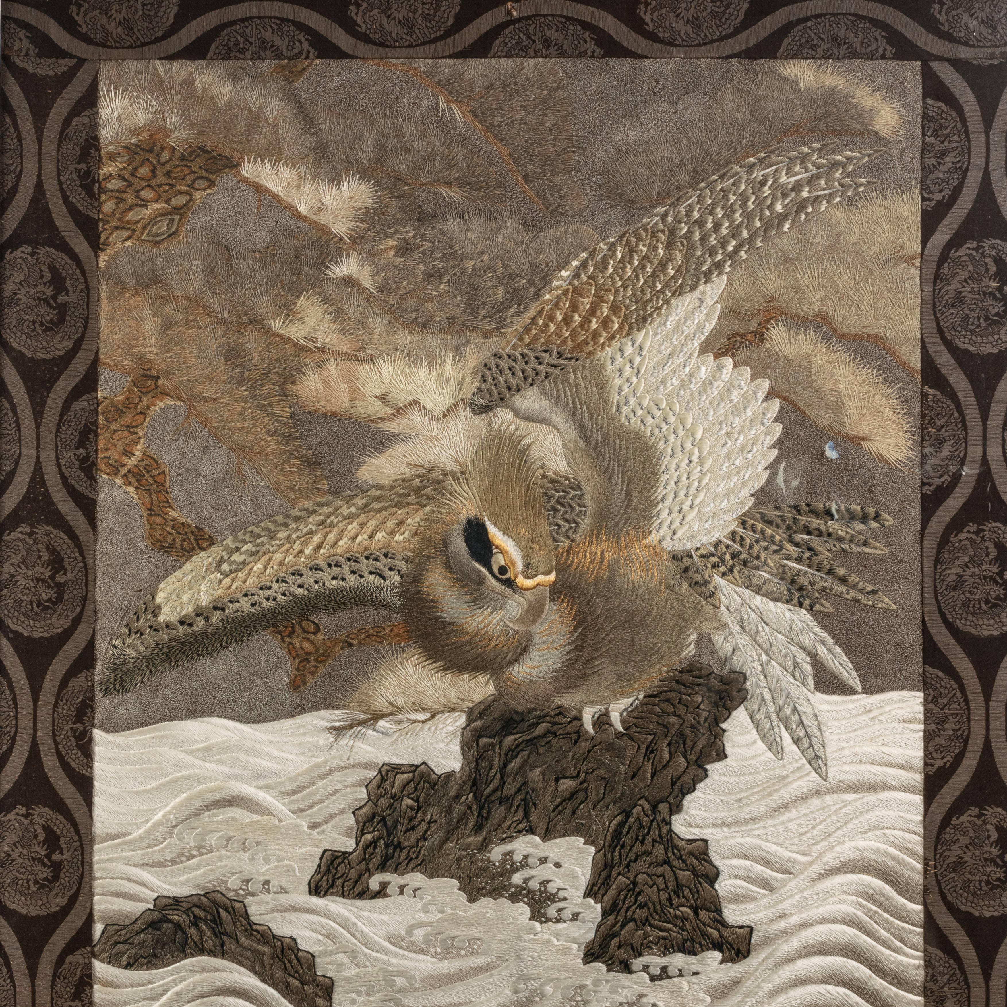 A large Meiji period silk embroidery of a sea eagle,
worked in a cream, brown and black palette with gold thread highlights, showing a sea eagle perched on a rocky outcrop scanning the frothing waves beneath him for fish, within a black brocade
