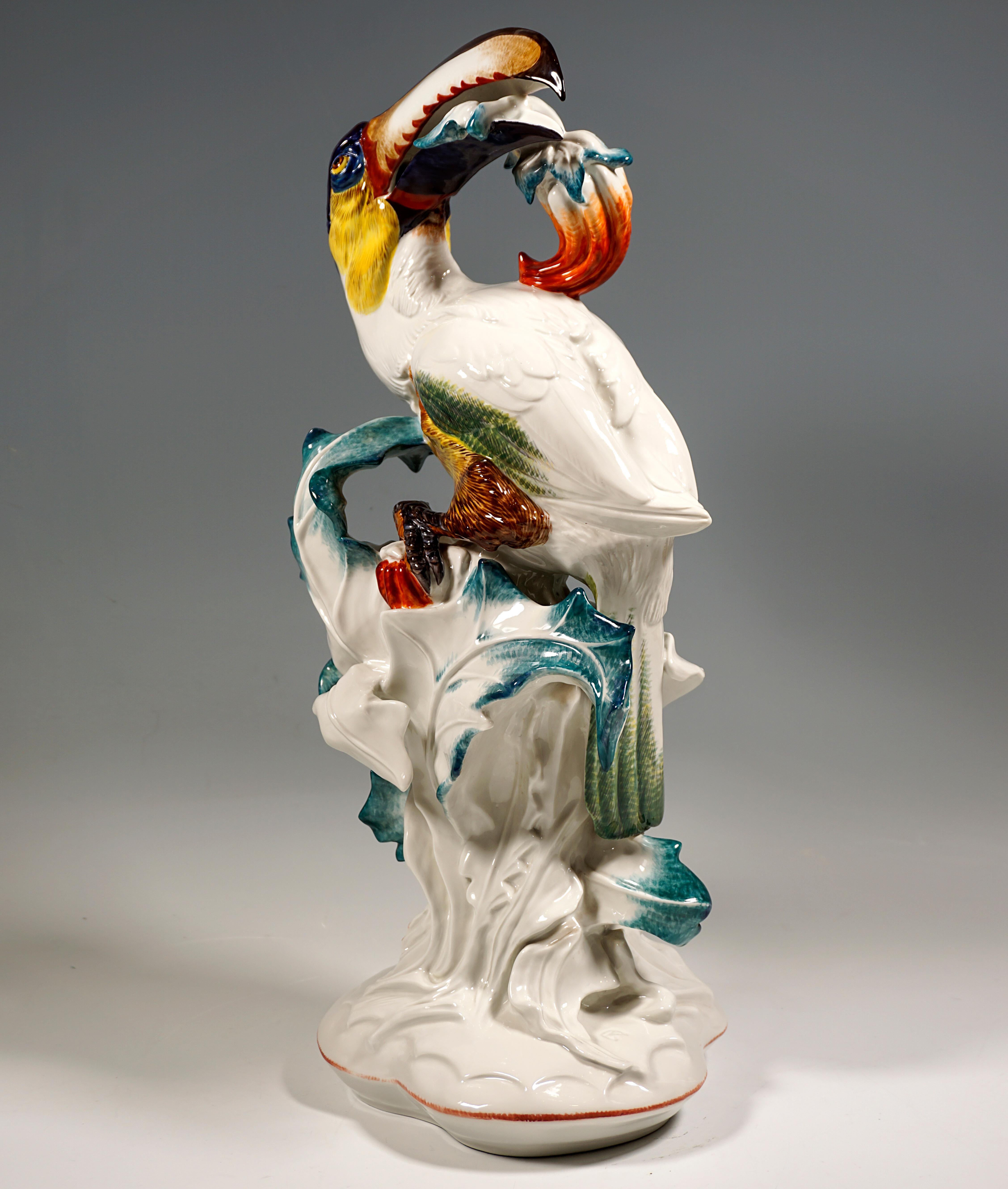 Highly decorative depiction of a life-size peppereater with its head turned backwards and a fruit in its beak, clinging to a leafy plant.
Painted with strong color accents, on a trefoil base with a red border and artist's mark 'PW' next to the tuft