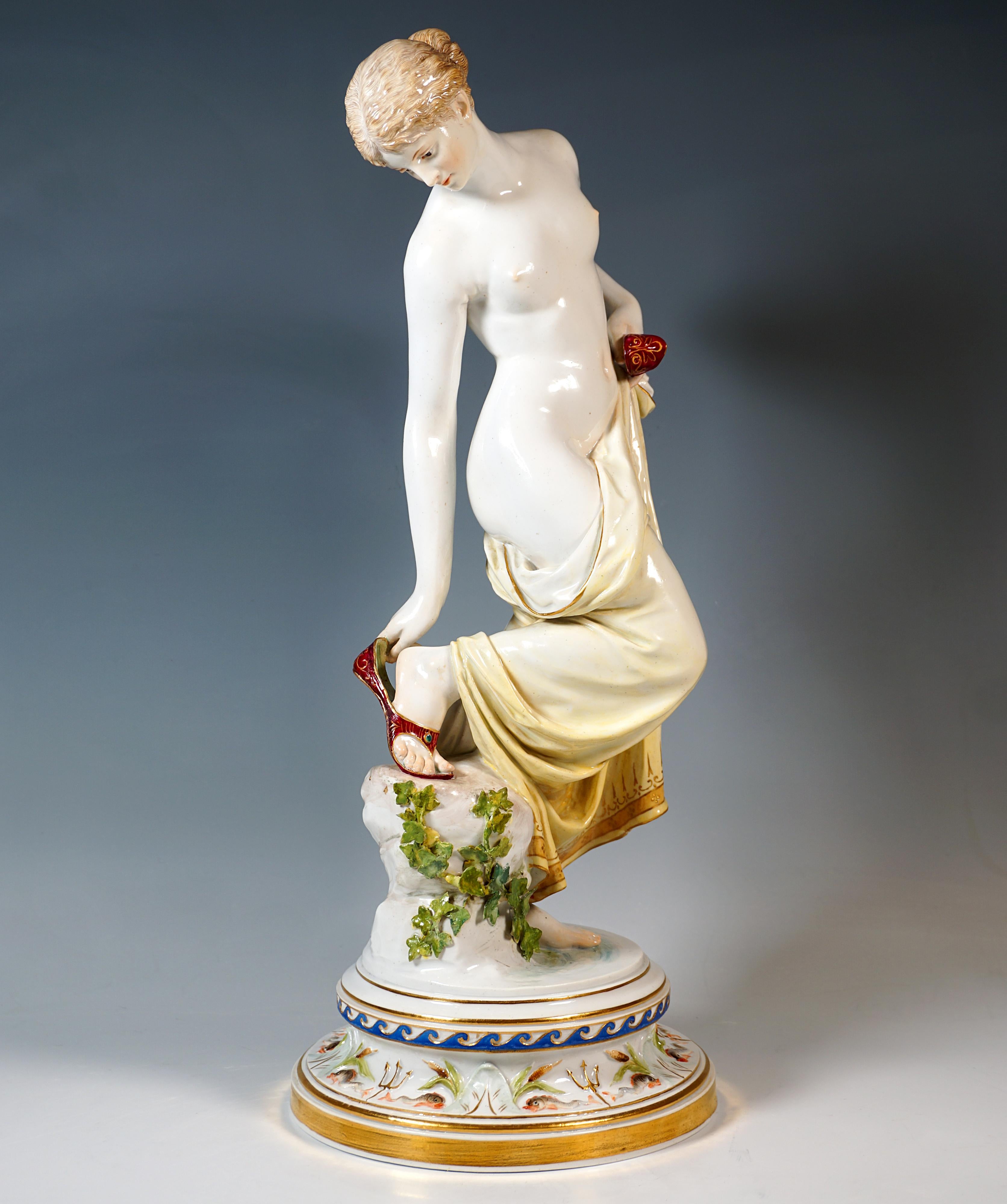 Représentation extrêmement décorative, entièrement sculptée, d'une jeune beauté nue, les cheveux attachés, couvrant sa nudité après son bain d'un tissu doucement drapé, qu'elle tient d'une main à sa hanche gauche, avec un 
Elle se glisse dans la