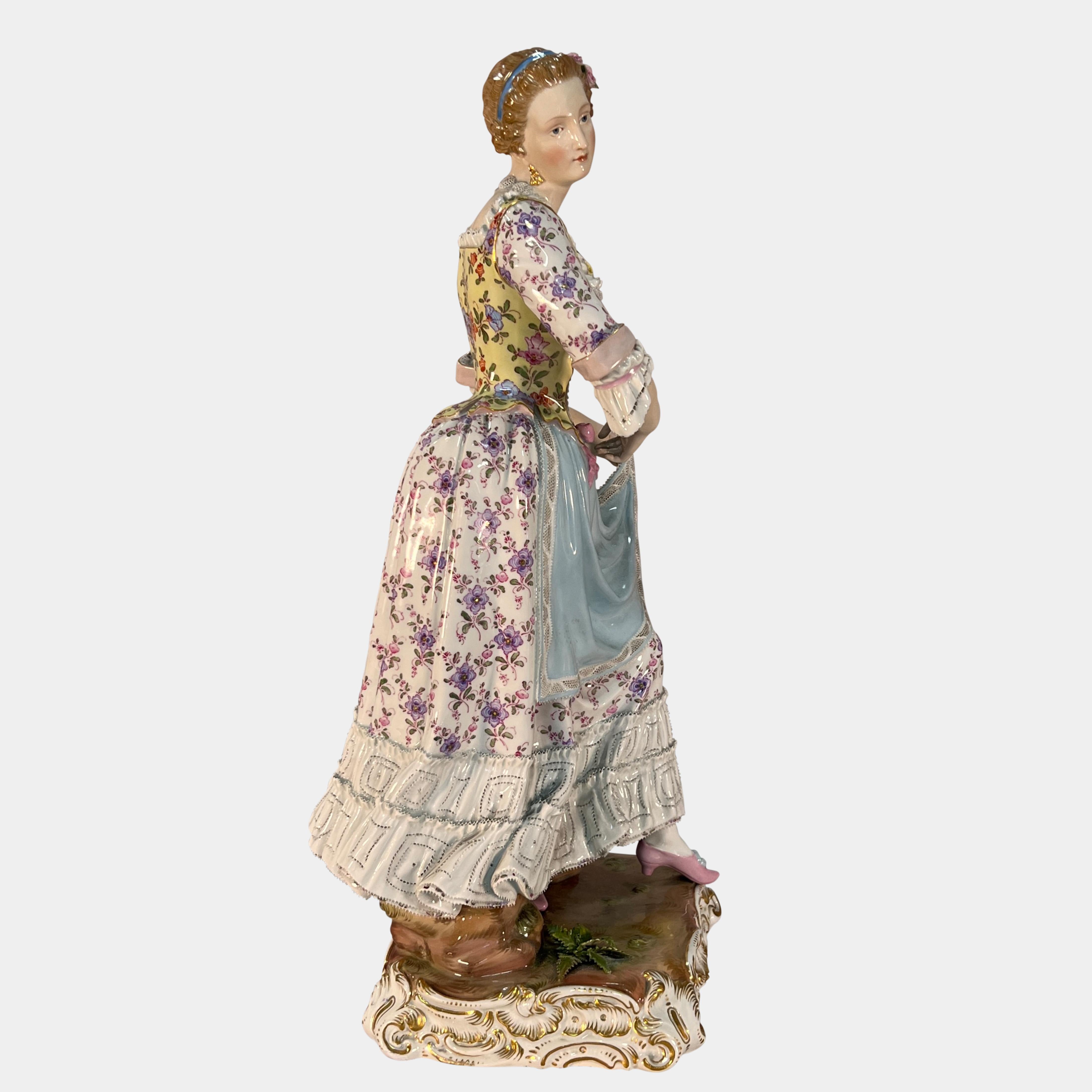 A beautiful large 19th century Meissen porcelain figure depicting a standing maiden in period dress with elaborate floral decoration raising her apron. her corset and borders made from fine dipped lace. The figure is supported by a rock and is based