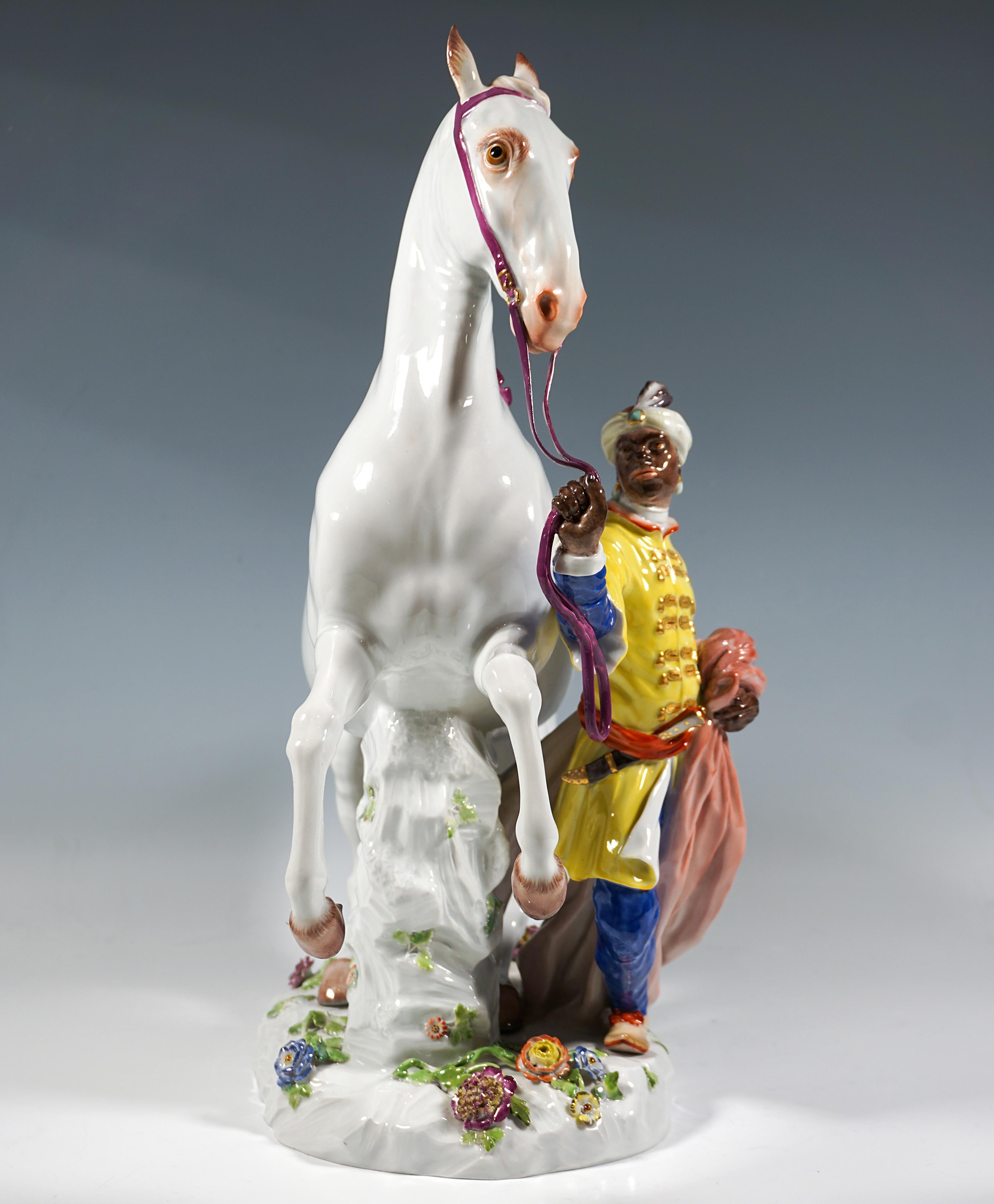 Depiction of a young man dressed in a colourful robe – blue shirt and trousers with a yellow frock coat – with a turban and earrings, a dagger stuck in his red sash, holding a red cape in his left hand and leading a magnificent 
rearing white horse