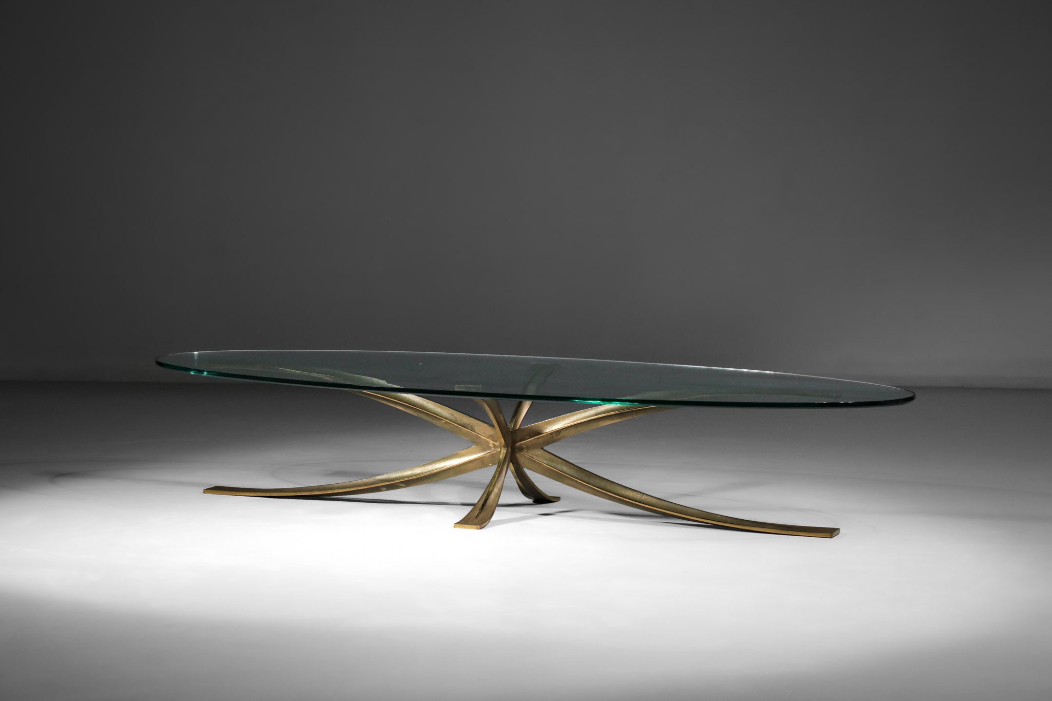 Rare oval coffee table by the French architect Michel Mangematin from the 60's (he created very few pieces of furniture during his career). Star base made of 4 gilded bronze blades and oval glass top, all original and in excellent vintage condition