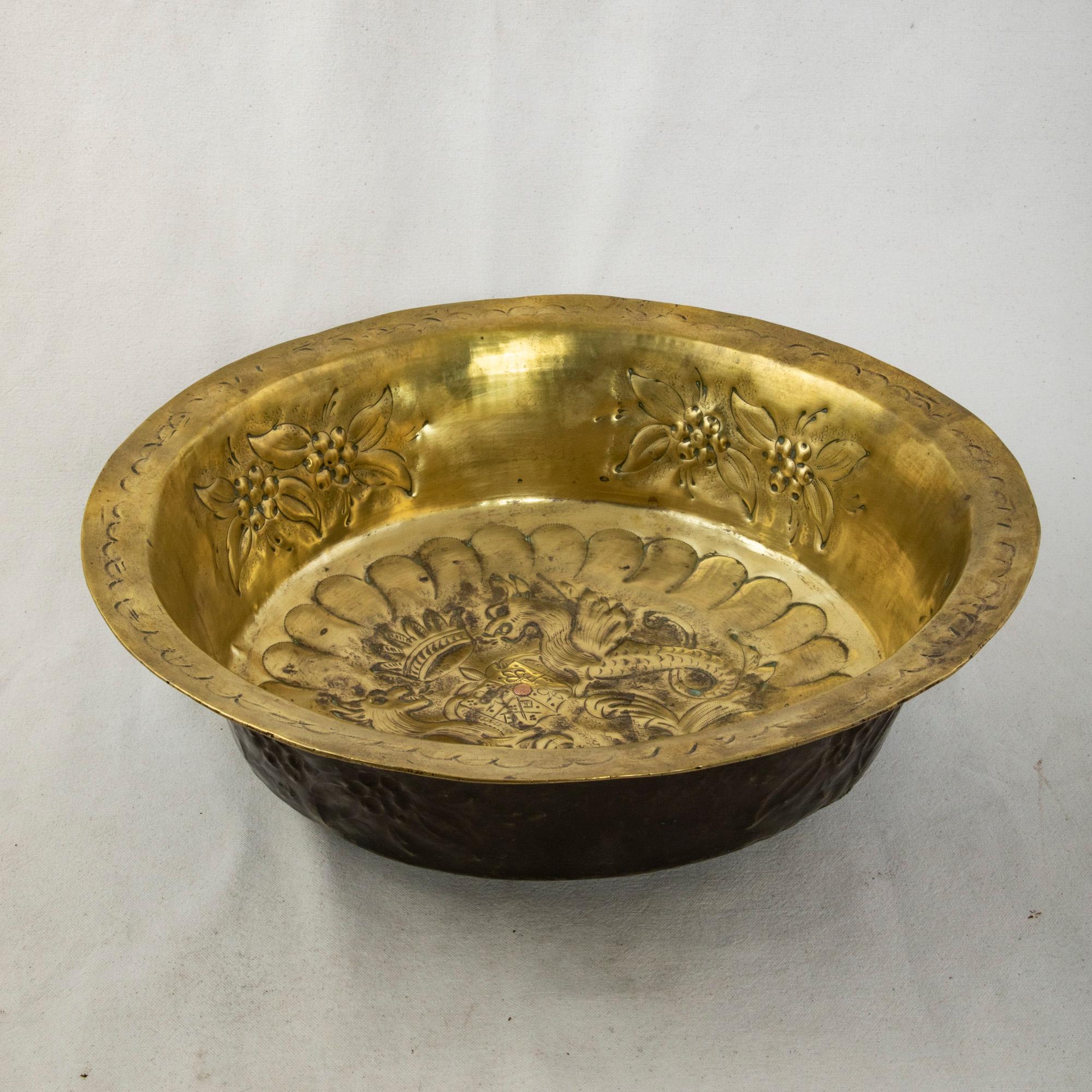 Originally used in a church as an offering plate, this mid-eighteenth century French brass repousse bowl features a coat of arms in the bottom displaying the fleur de lys of France and the ermine of Brittany. A crown rests above the coat of arms,