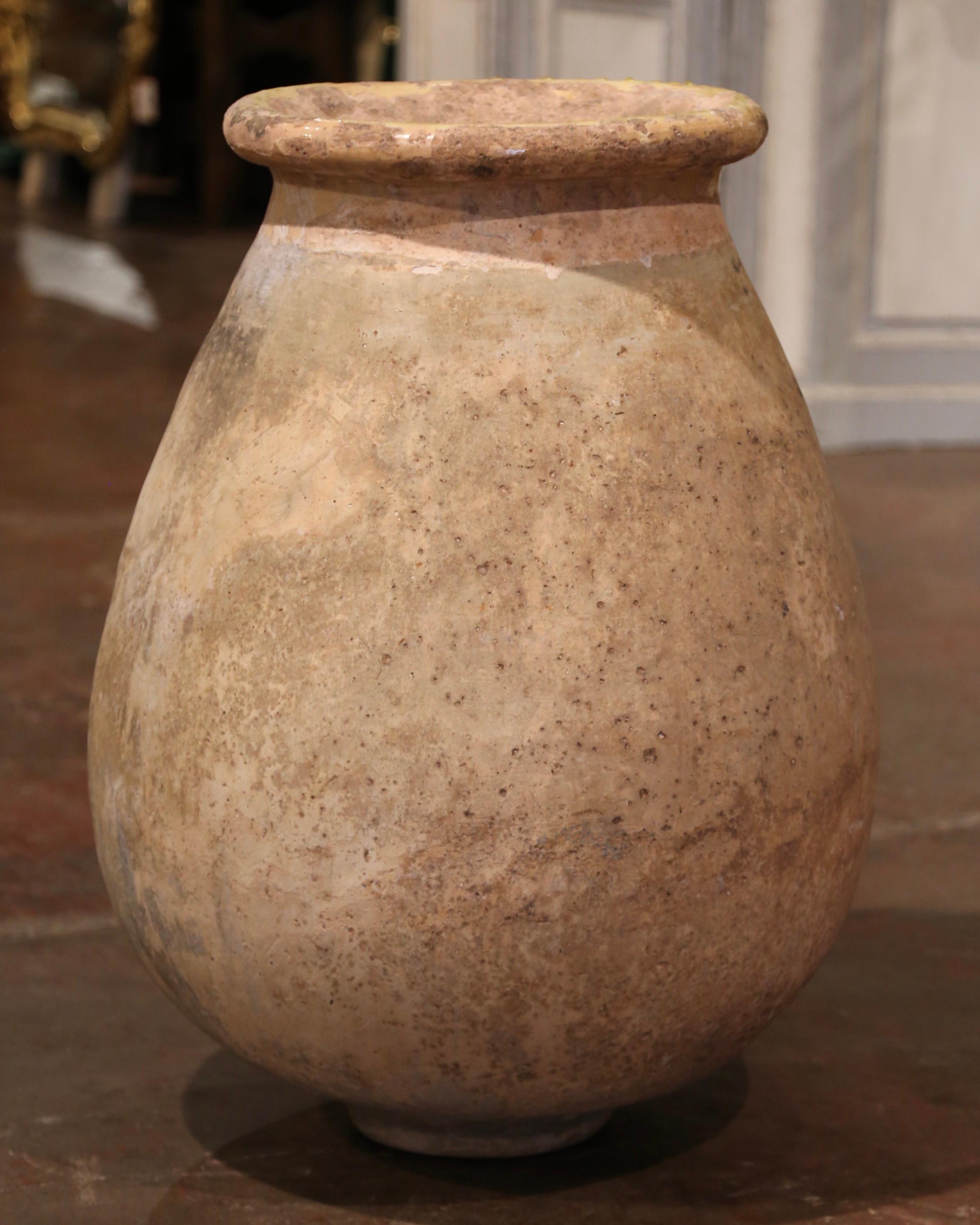 This large, antique earthenware olive jar was created in Southern France, circa 1850. Made of blond clay and neutral in color, the terracotta vase has a traditional round shape. The rustic, time-worn pot features a yellow glaze around the neck and