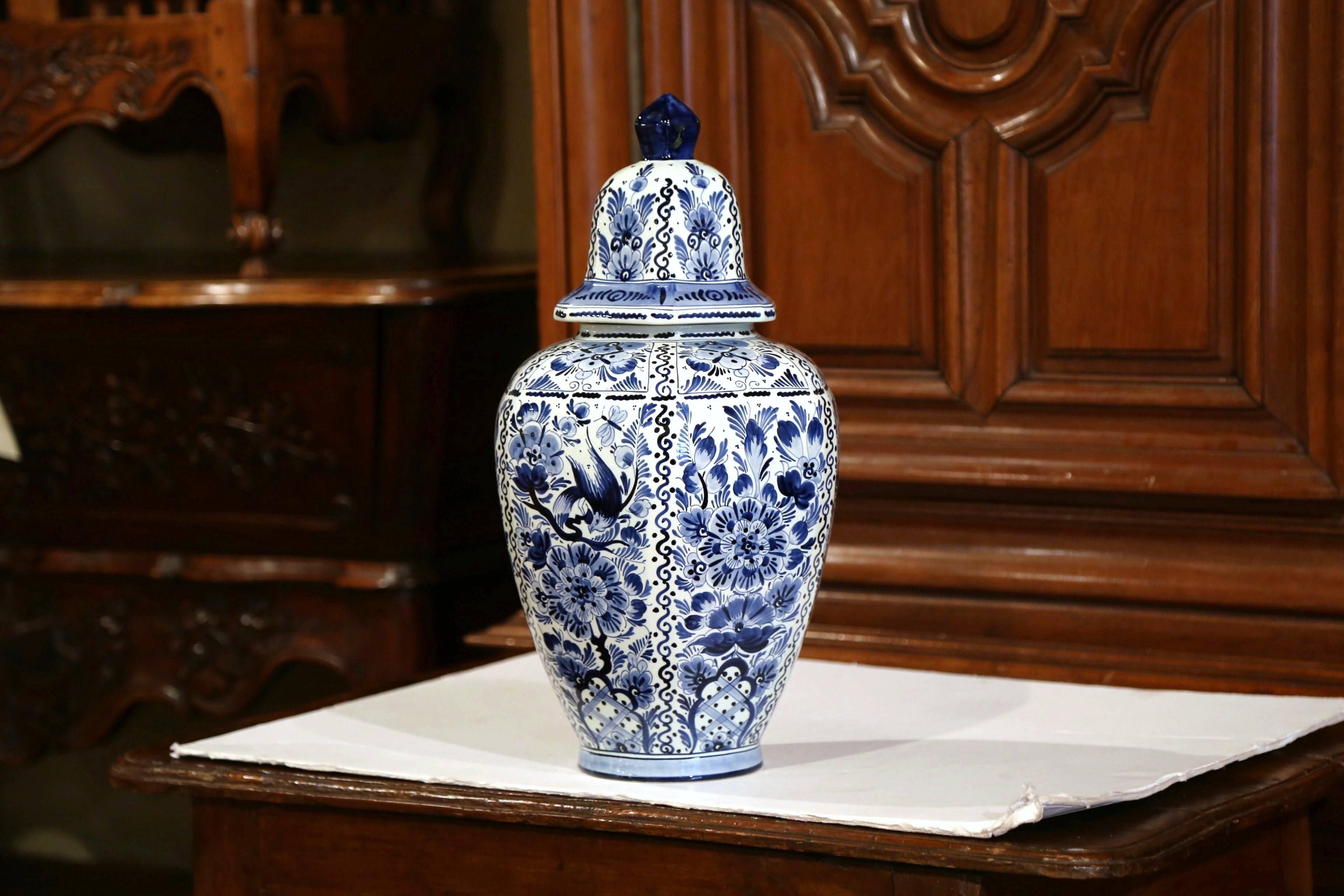 This large and elegant vintage ceramic ginger jar was created in Holland, circa 1950. The mid-century faience potiche features hand-painted Dutch flowers and foliage. The traditional blue and white jars have a dome shaped lid at the top, and are