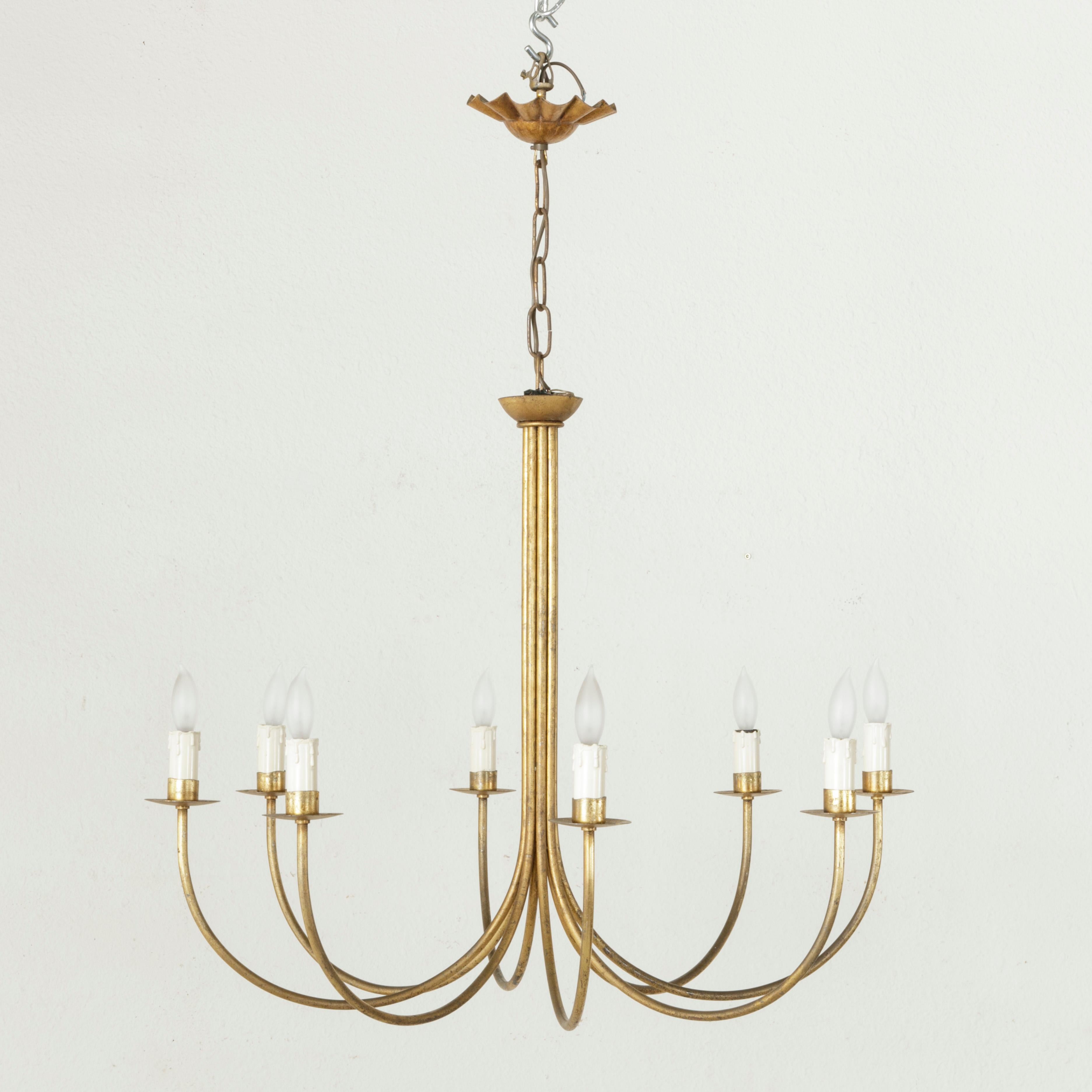 This large midcentury French gilt metal chandelier features a simple design with eight curved arms that join together to form a central pillar. Each arm curves up and supports a bobeche and single light. This circa 1960 chandelier is wired to