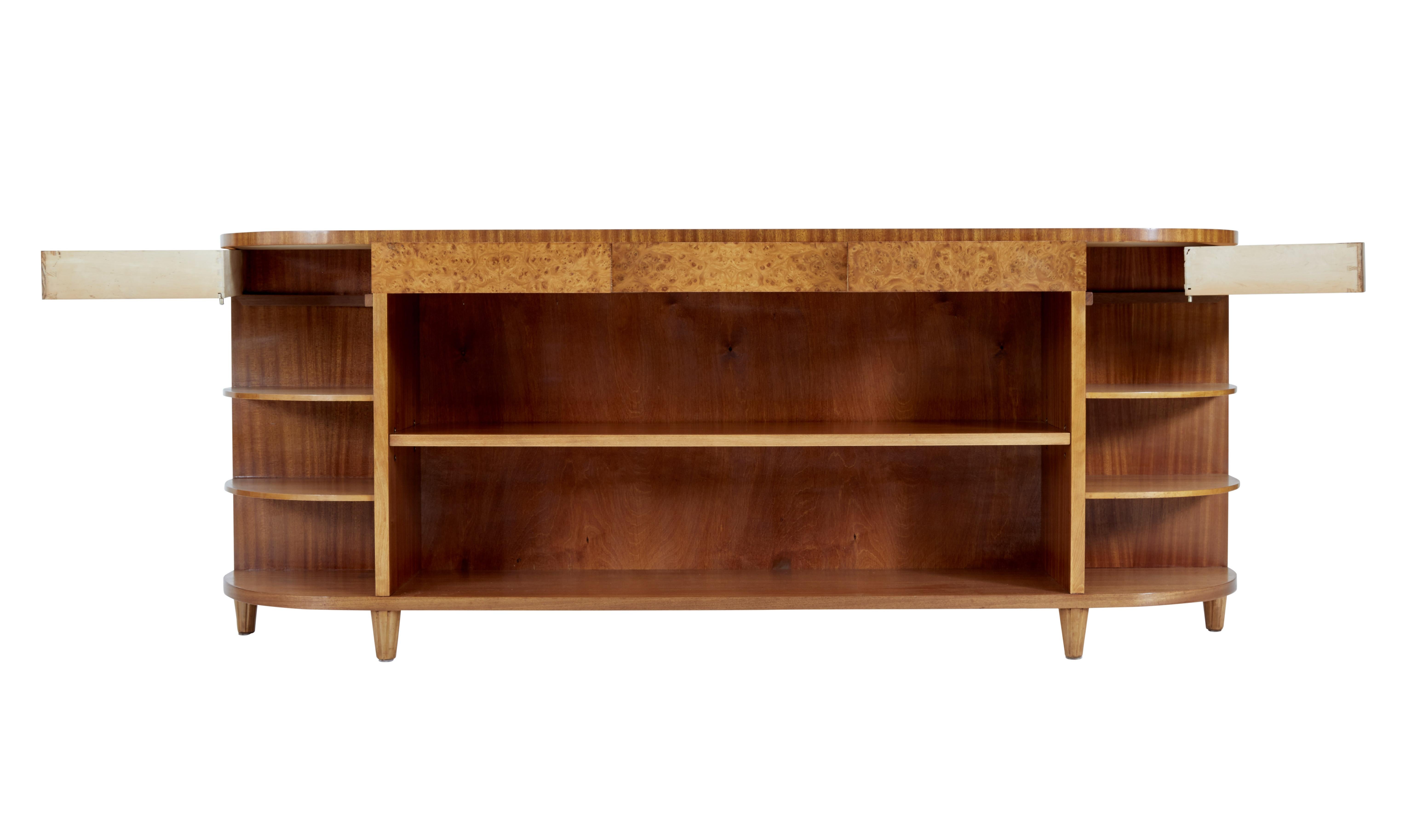 Large mid 20th century Scandinavian low open mahogany bookcase circa 1960.

Good quality shaped low open bookcase. Matched veneer top with 3 burr drawers below the surface and 2 swing out drawers on each end. Main storage area with a single