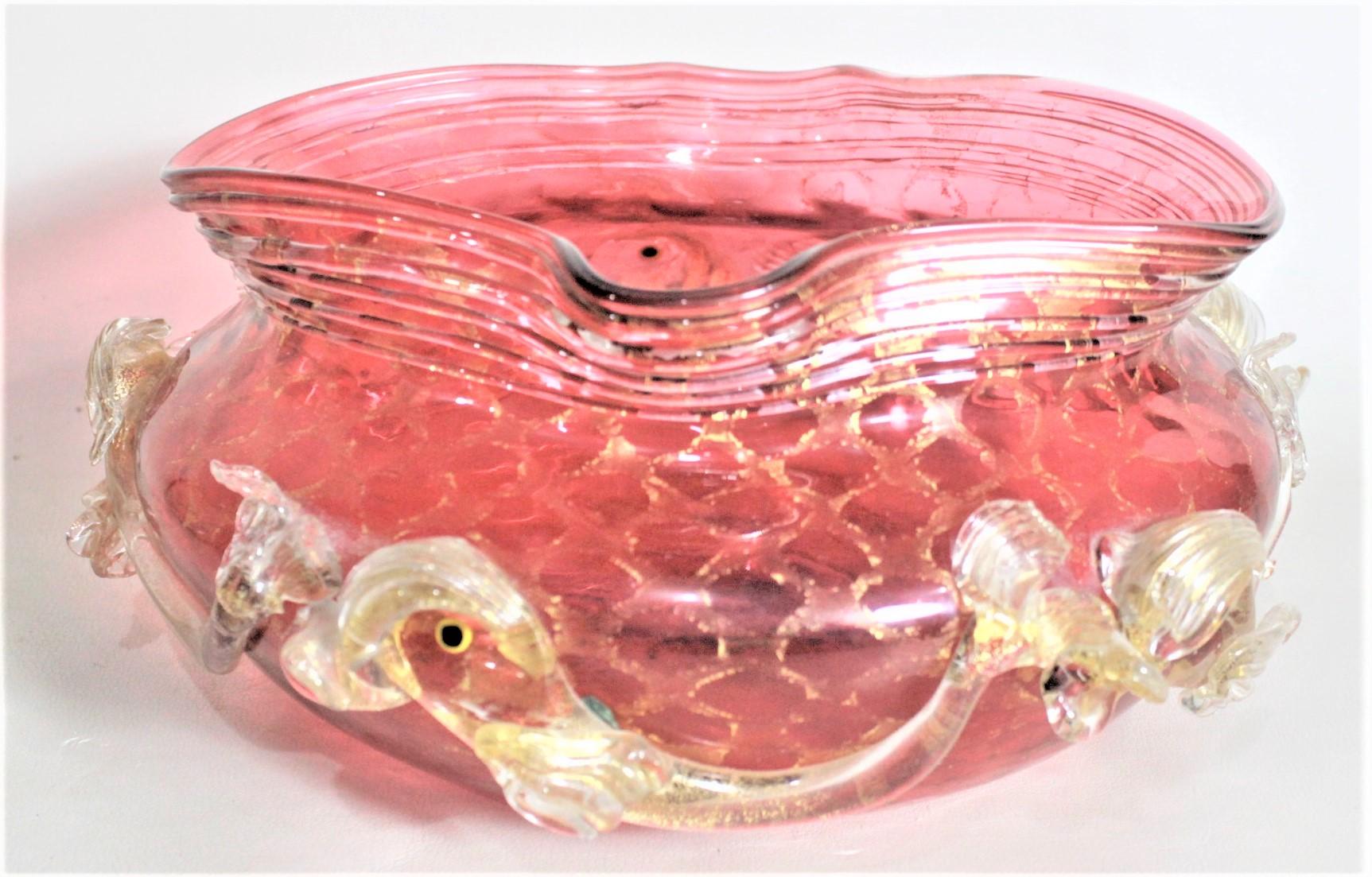 This early Murano art glass bowl is unsigned and unattributed, but presumed to have been made in Italy in approximately 1950 in the period Mid-Century Modern style. This crimped bowl is done in cranberry glass with a series of applied figural