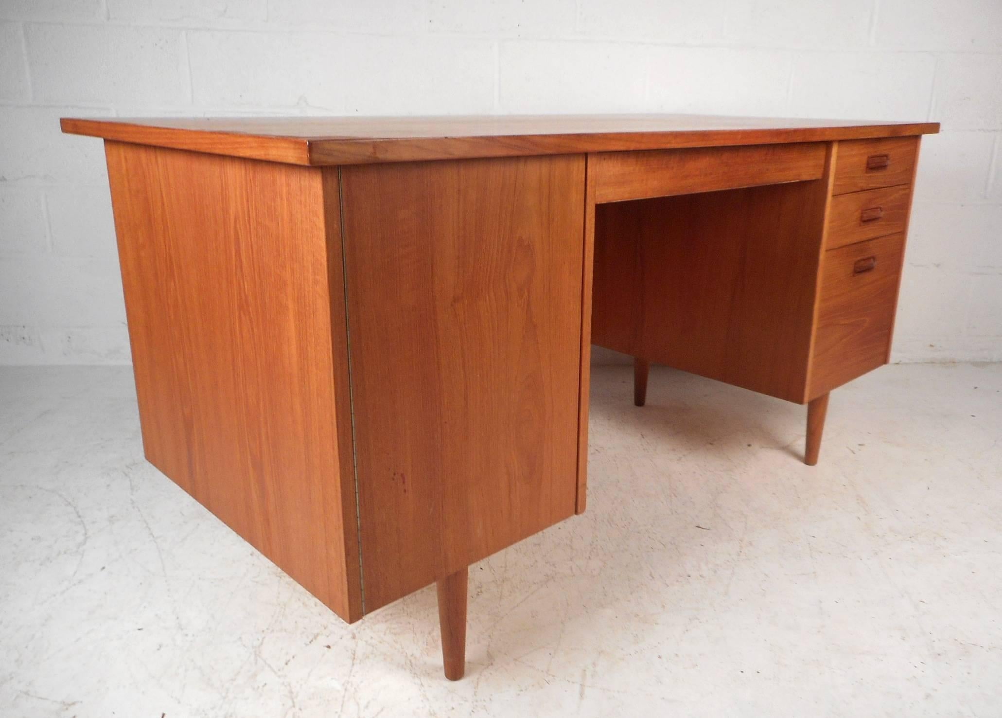 This impressive vintage modern desk features plenty of work space on its 58 inch wide by 29 inch deep top. This beautiful case piece offers plenty of room for storage within its hidden compartment with a shelf, middle drawer, and three side drawers.
