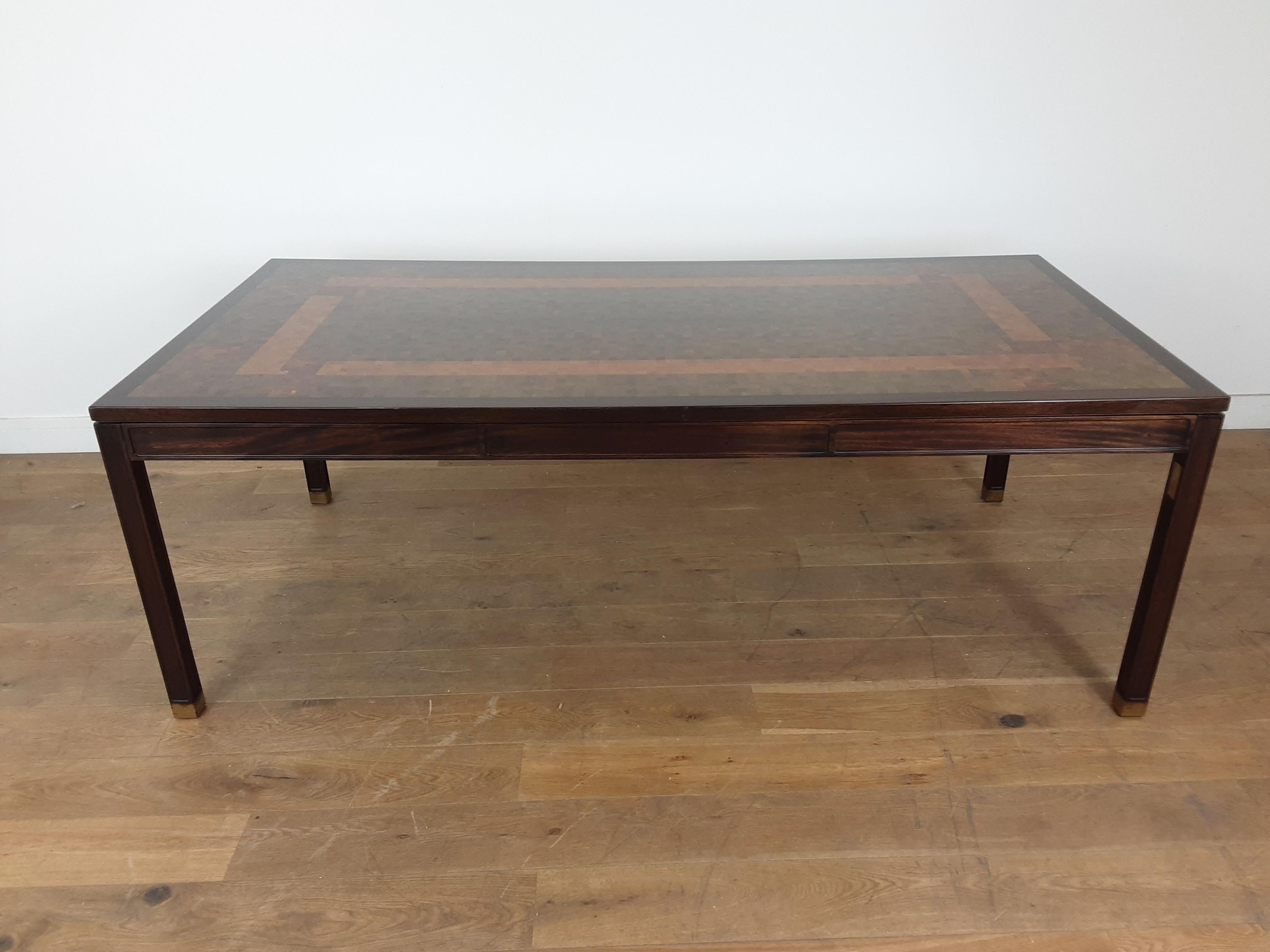 Stunning large midcentury dining or work table with beautiful fruit woods forming a mosaic and cross band design.
in a strong and paneled mahogany frame the feet finished with polished brass.
produced by Tranekaer furniture with brass plate