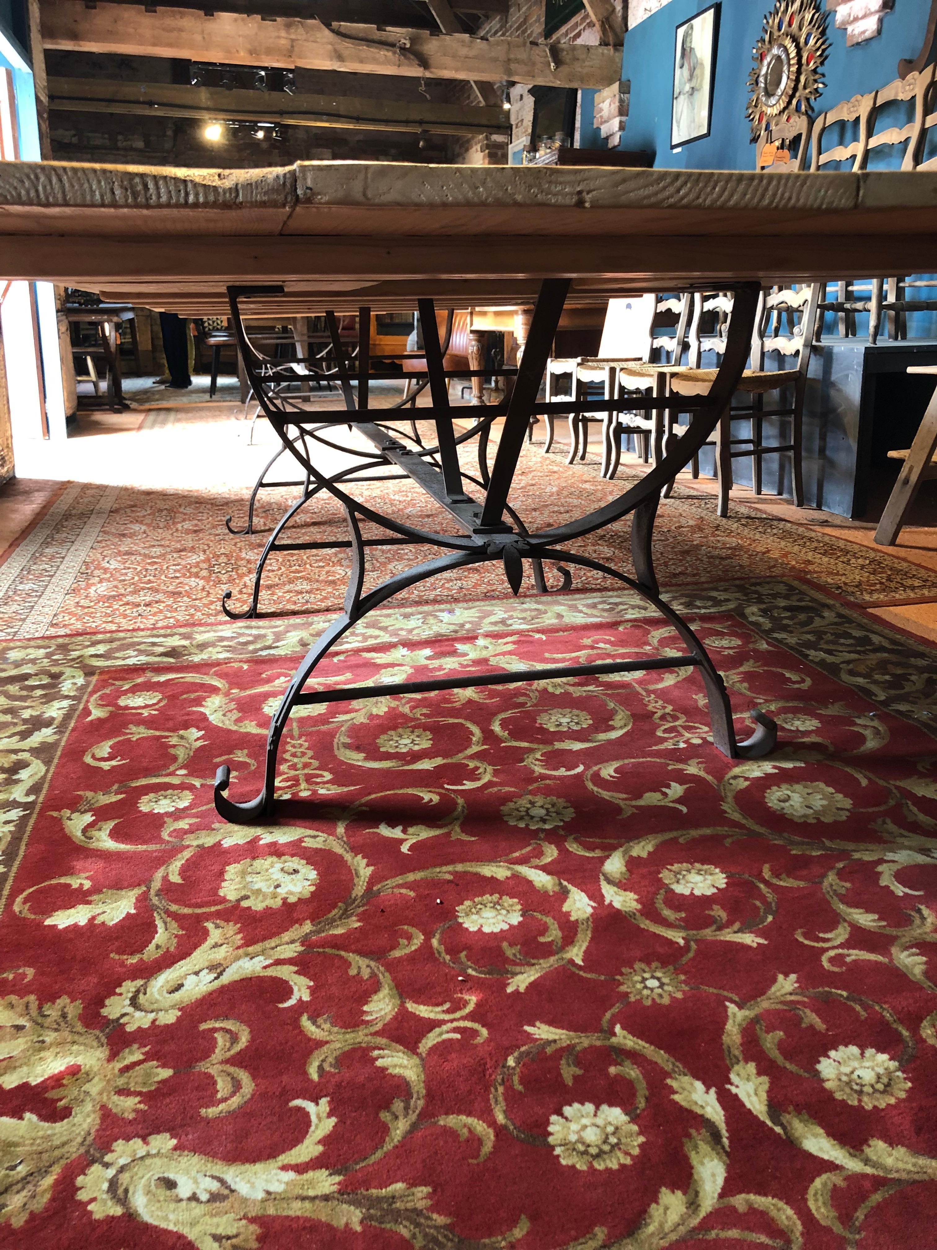 A very large rustic midcentury Dutch pine dining table with a handmade iron base with fleur-de-lys decoration.

This tabletop was taken from an old Gouda cheese factory in Holland. One can still see where the Wheels of Cheese were left to age. The