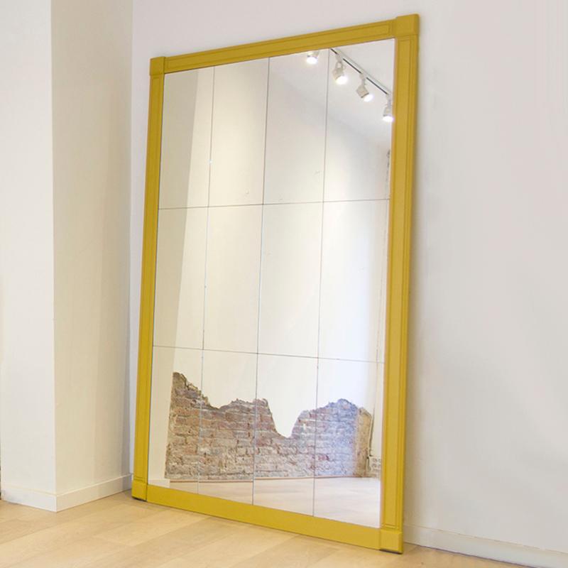 This large statement floor mirror is made of nine smaller sections of mirror placed together. The outside wood framing has raised square corners and the sides have linear grove detailing. A golden yellow has been painted over the framing to add a