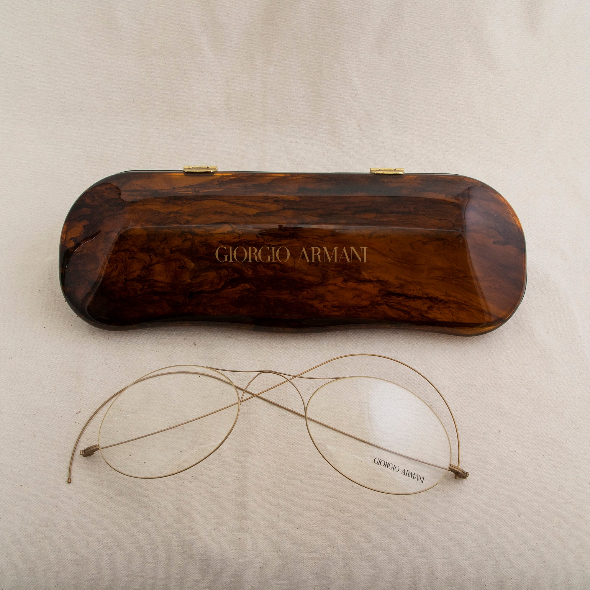 This very large mid-twentieth century French faux tortoise shell glass case factice features a pair of large wire rim glasses. Both the case and glasses are marked Georgio Armani. The case measures 18.5 inches long by 6 inches wide and 4 inches