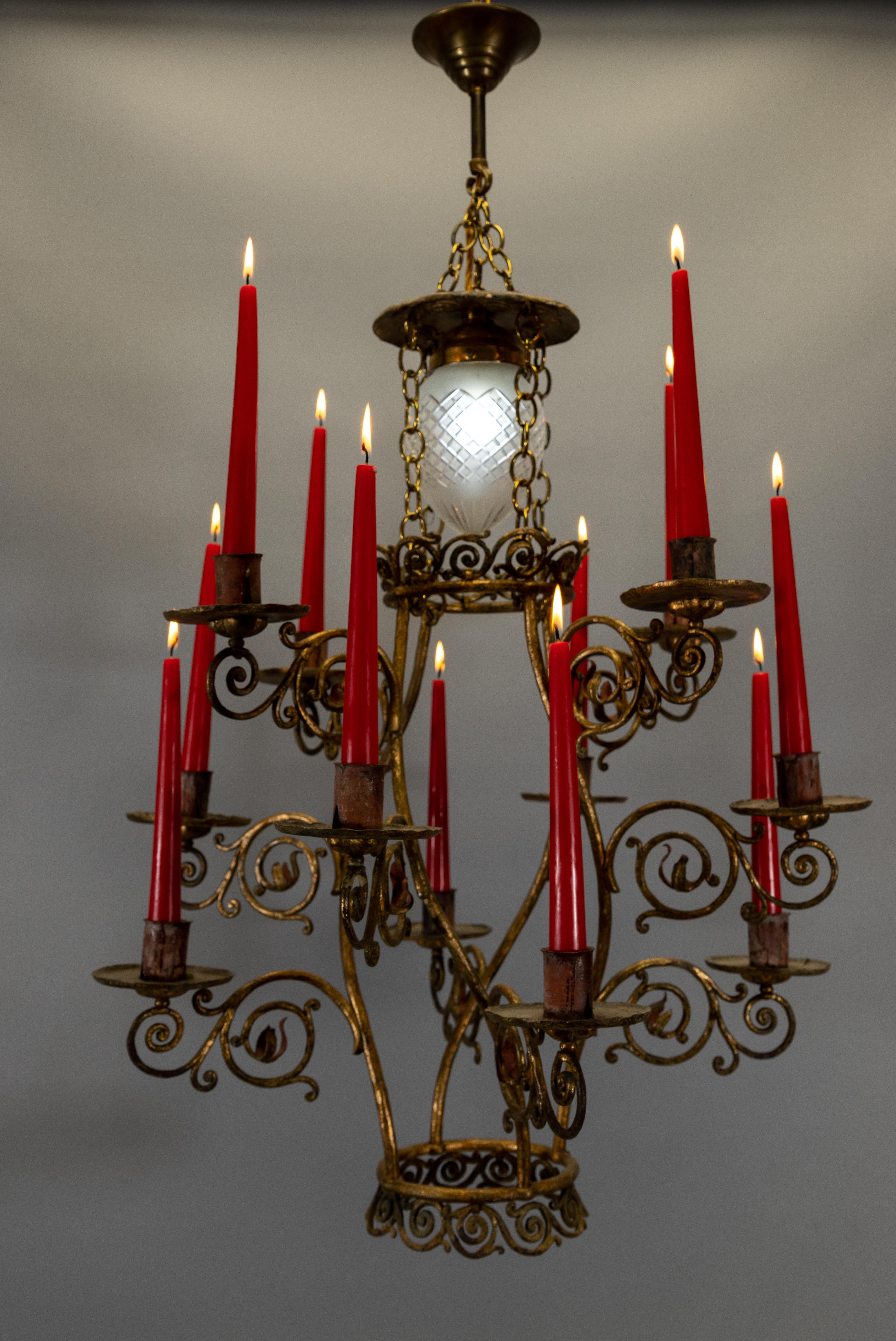 Un suggestivo e scultoreo lampadario a candela in ferro dorato francese della metà del XX secolo, con dodici candelieri disposti in una graziosa composizione a gradoni. Il design di questo lampadario combina un'ornata decorazione a volute in ferro