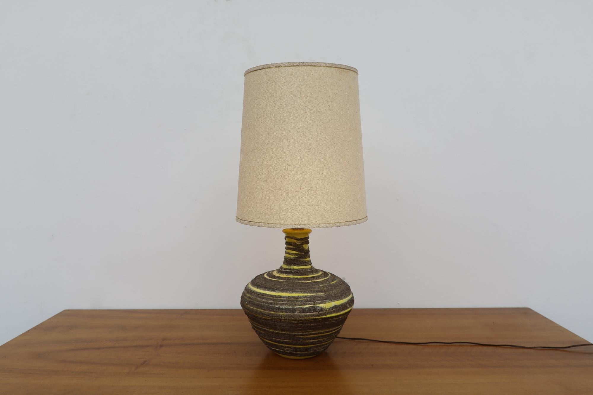 Lampe de table en céramique du milieu du siècle, joliment émaillée à la lave dans un tourbillon jaune et gris. Avec l'abat-jour d'origine. Dans un état général impressionnant, avec une certaine usure visible correspondant à son âge et à son