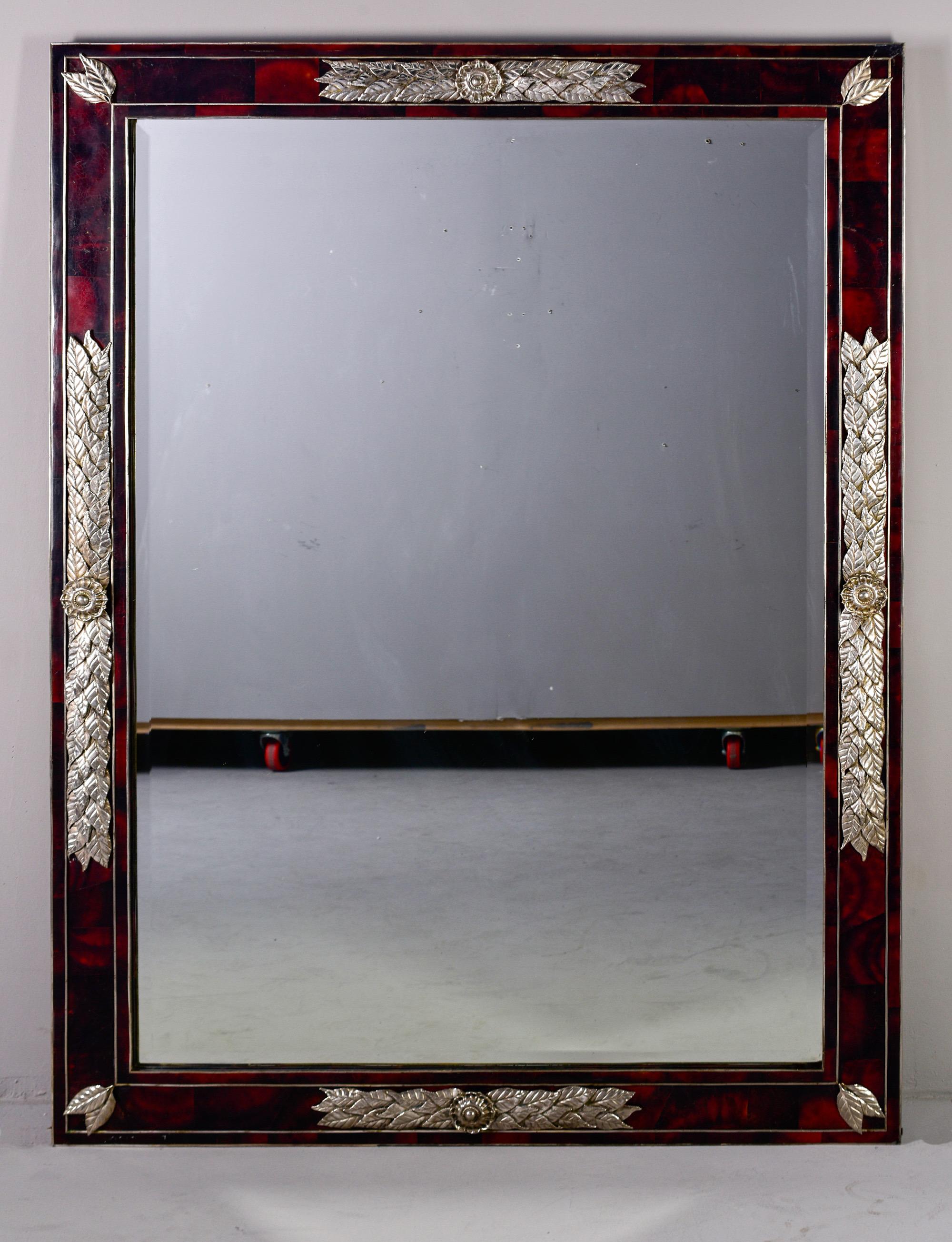 Circa 1980s large designer mirror features a frame of faux tortoise patterned glass that is embellished with silver plated floral mounts. The mirror has a beveled edge and is quite heavy and substantial. Mirror can be hung vertically or