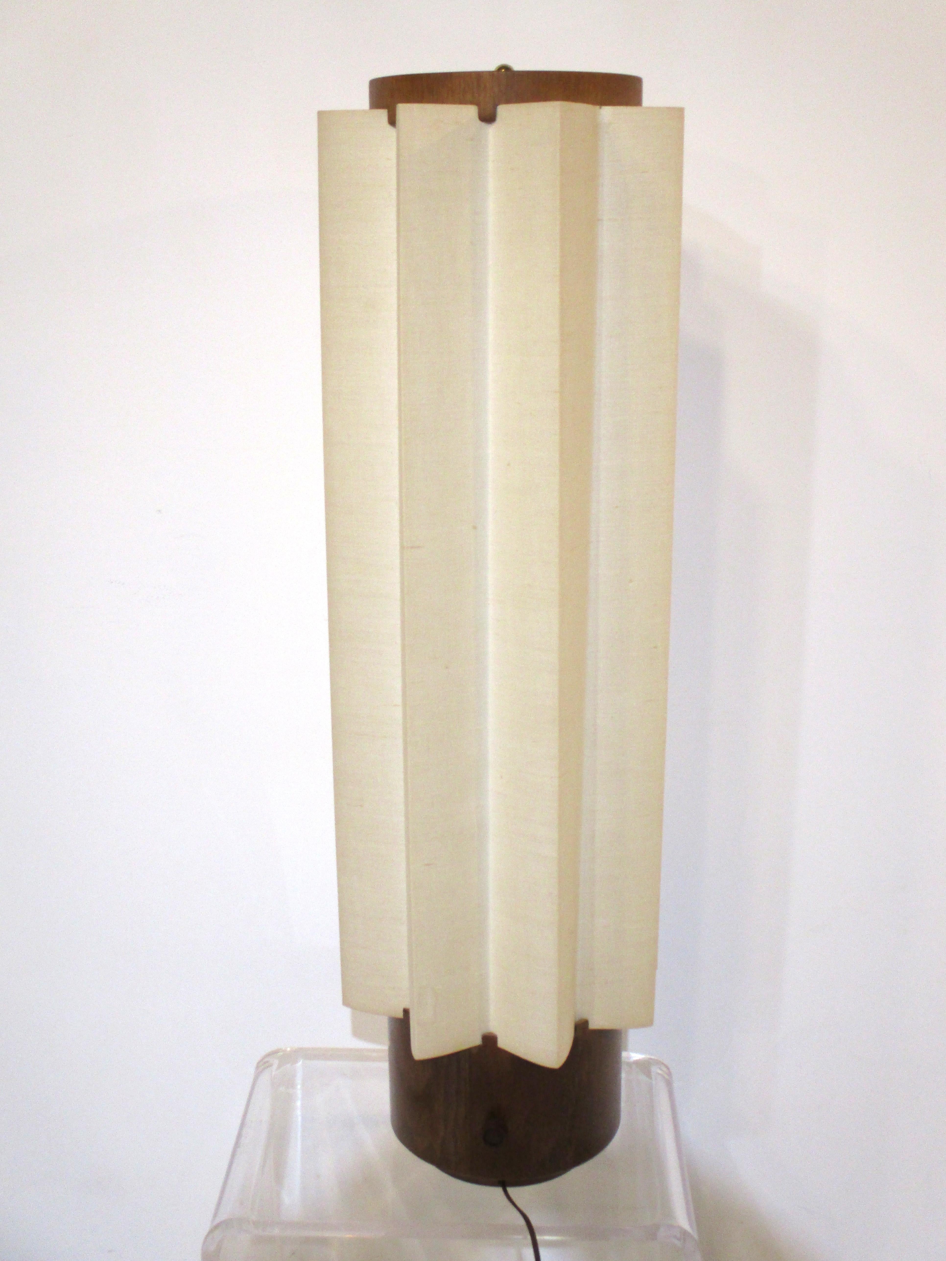 A larger sized mid century table lamp with pleated linen shade and round walnut base having a turn switch to the backside , the top has a round walnut piece with a opaque plastic defuser and round brass final. This well crafted lamp has wood slots