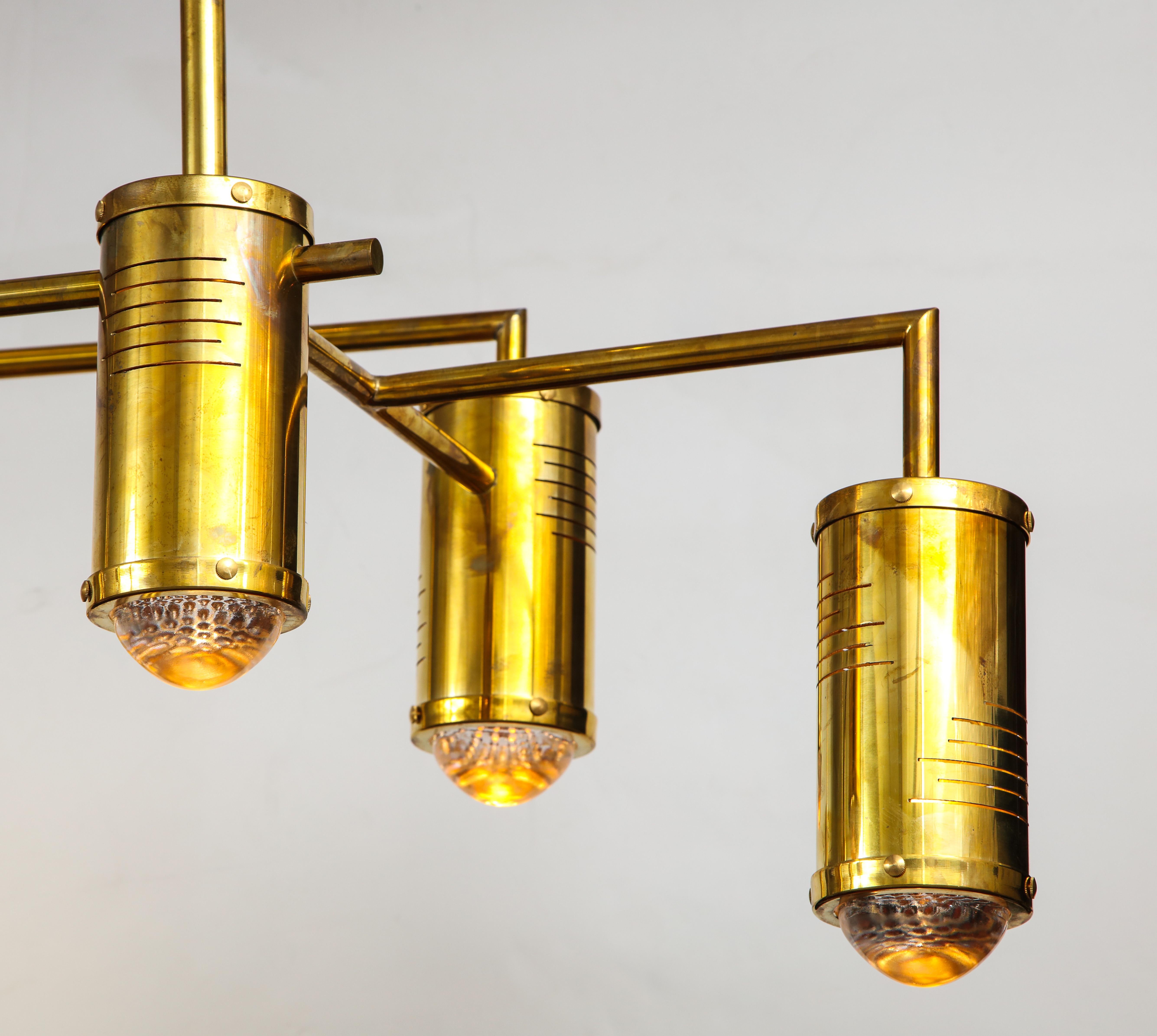 This Italian mid-century modern linear solid brass chandelier is the epitome of chic. Linear natural brass 9-arm frame features cylinder brass lights on multiple levels. Measures 5 ft. wide. Newly wired for U.S. standards utilizing LED lightbulbs.